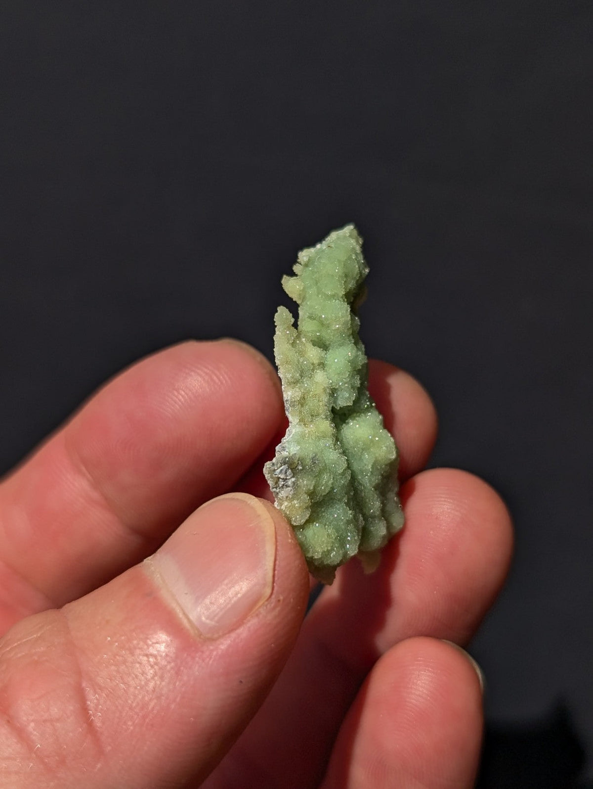 A pale green, crystalline mineral specimen with a rough, textured surface held between fingers.