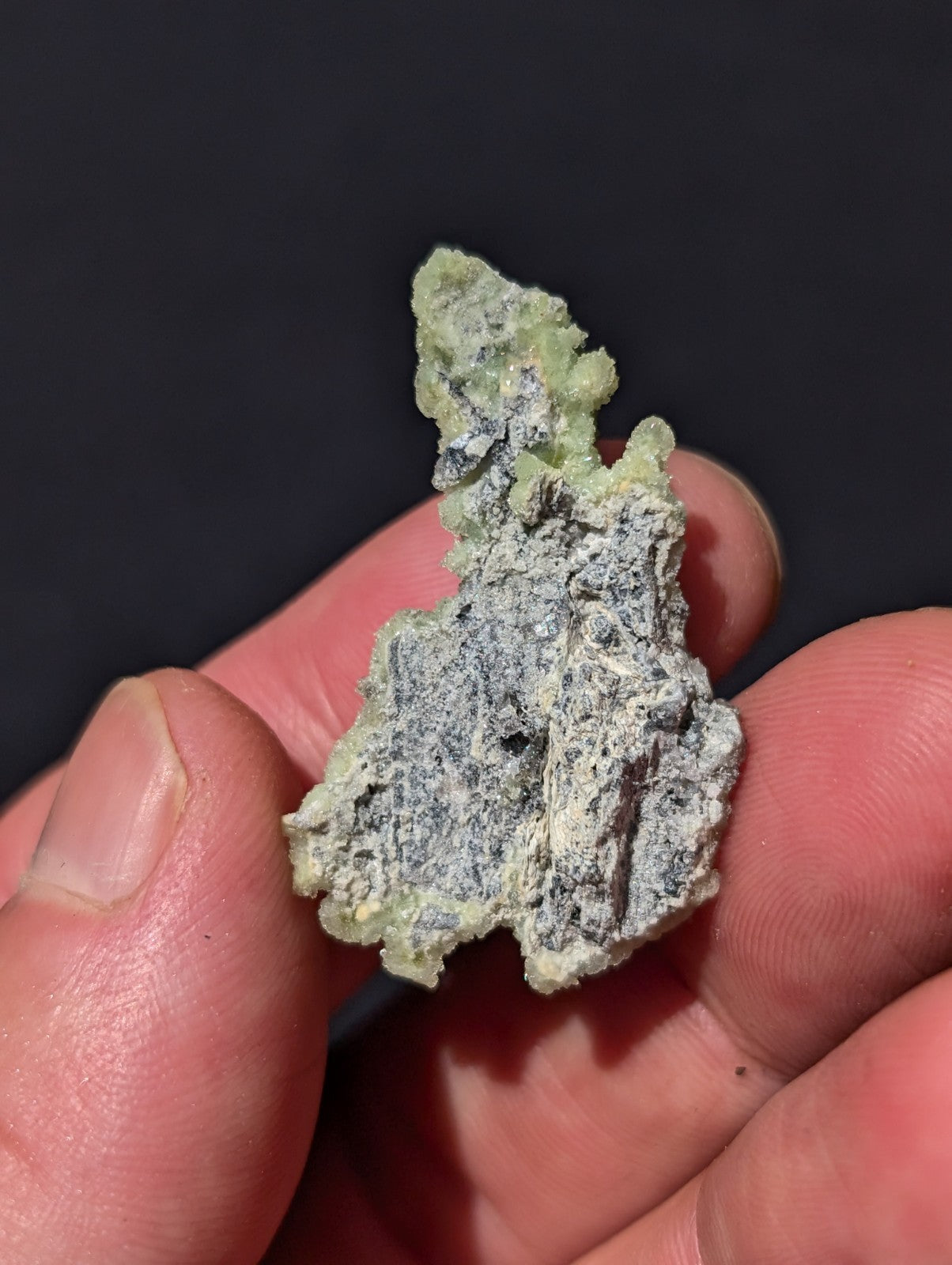 A rough, irregularly shaped mineral specimen with a pale green crystalline surface overlying a grayish matrix.