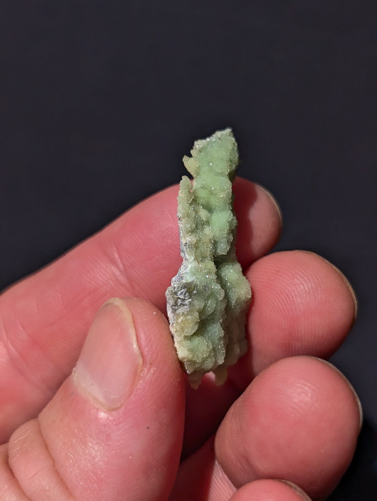 A pale green, crystalline mineral specimen with a rough, textured surface held gently in someone’s hand.