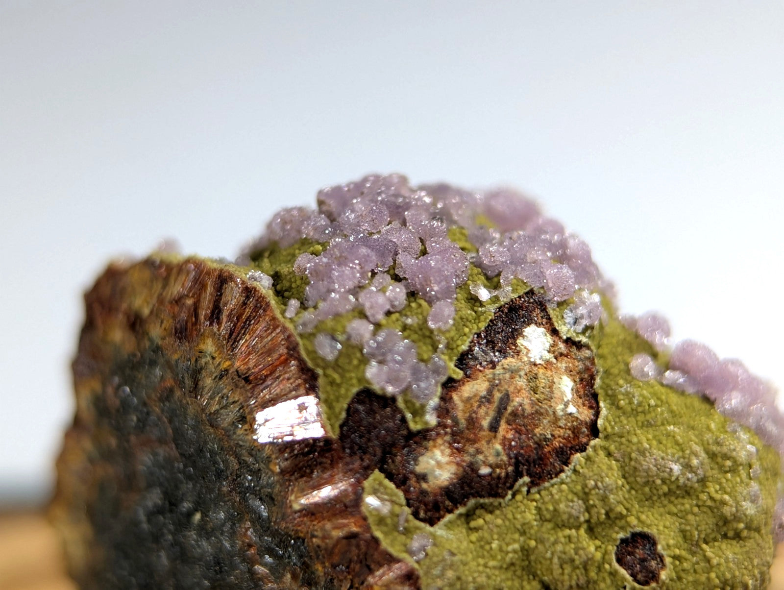 A vibrant green mineral specimen topped with clusters of translucent lavender crystals.