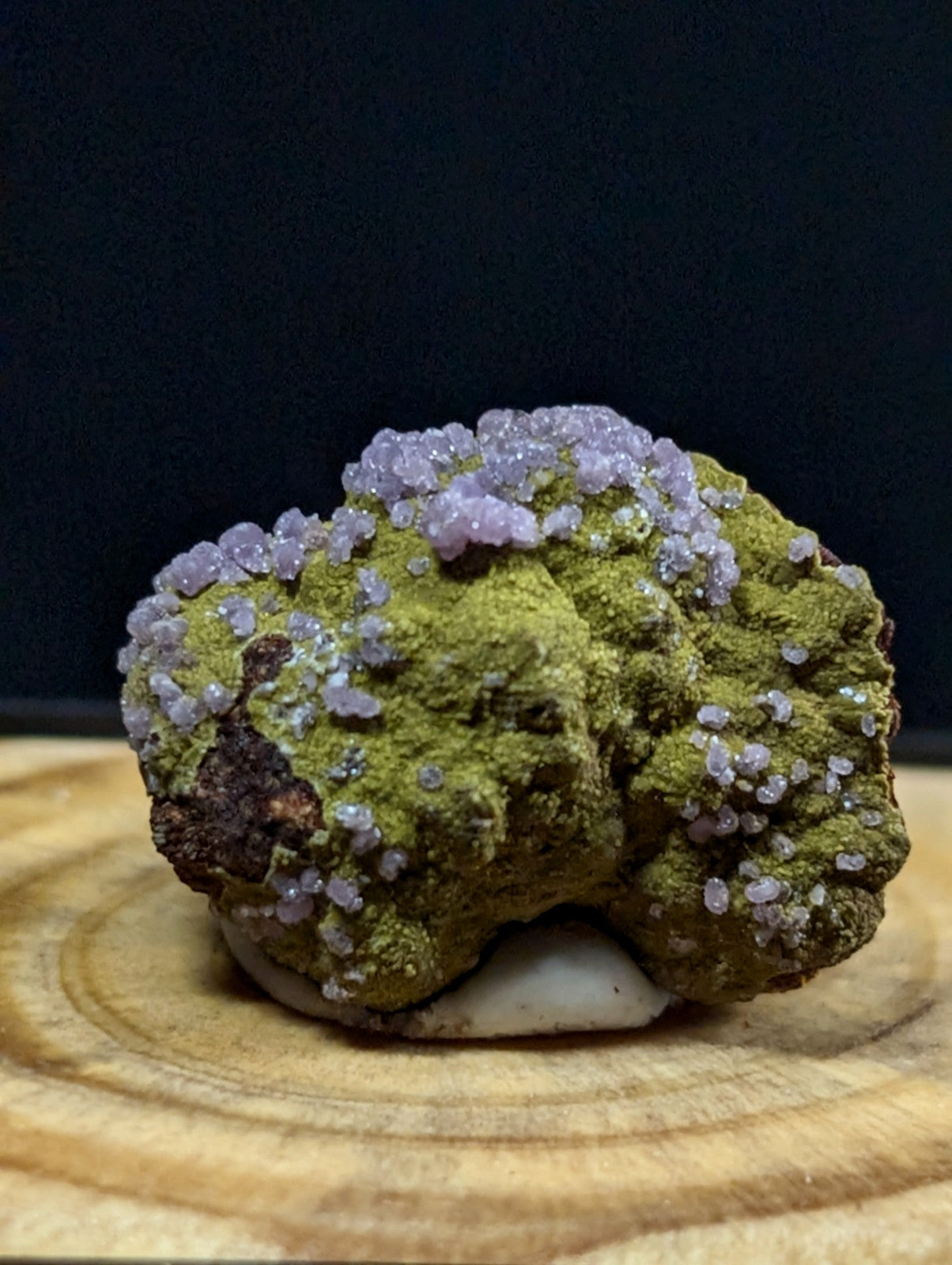 A vibrant green mineral specimen adorned with delicate, crystalline purple formations.