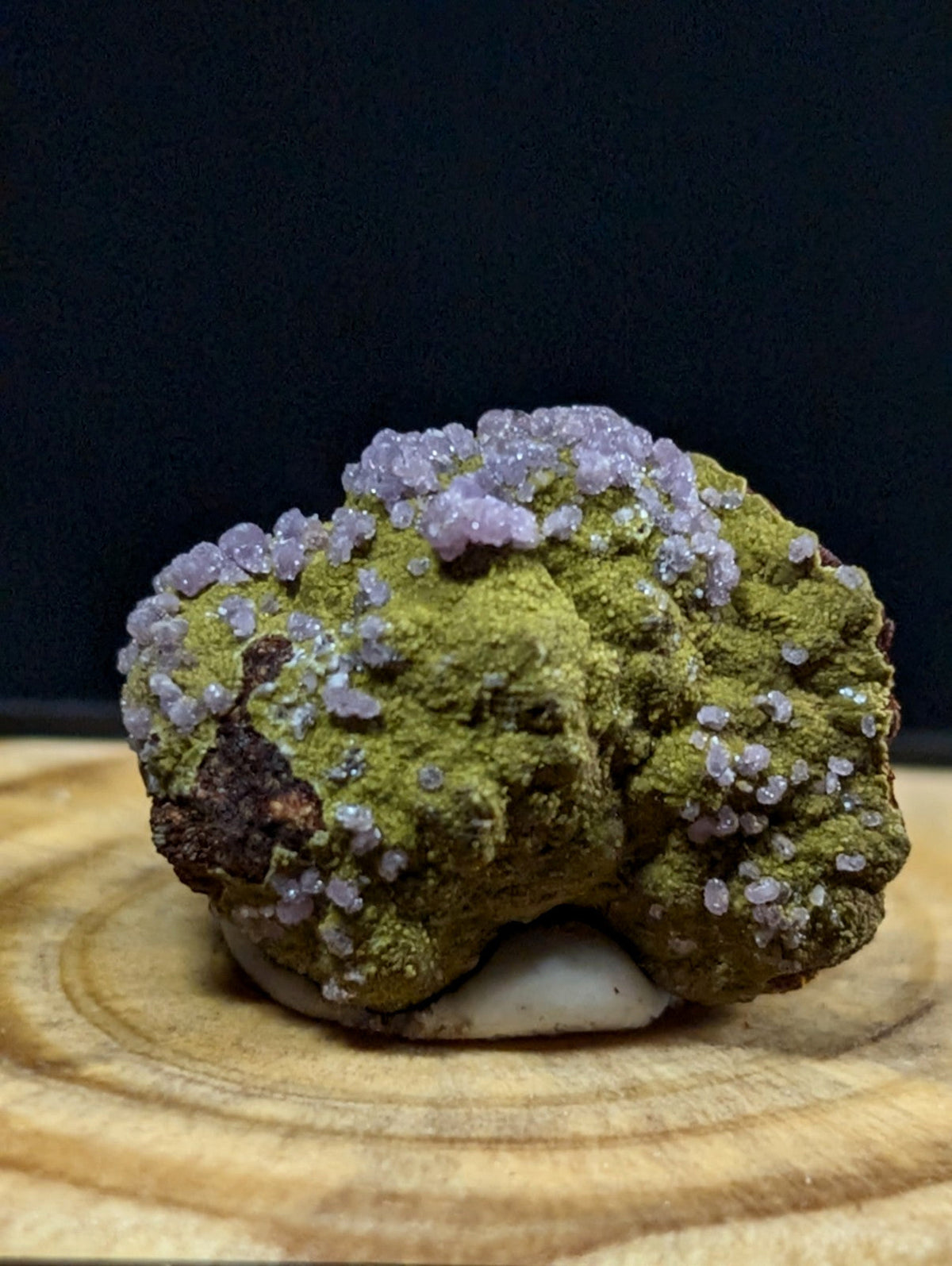 A vibrant green mineral specimen adorned with delicate, crystalline purple formations.
