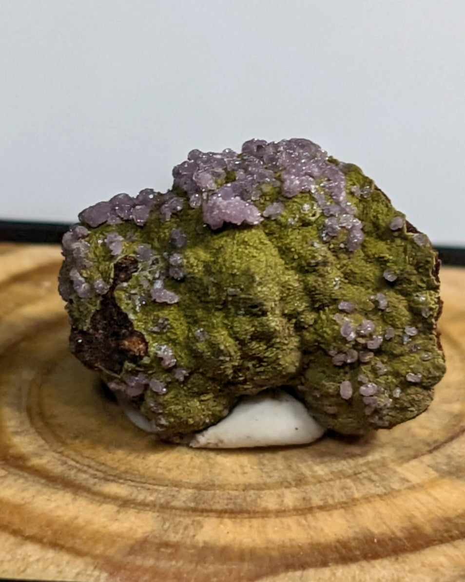 A mossy green mineral specimen topped with clusters of translucent purple crystals.