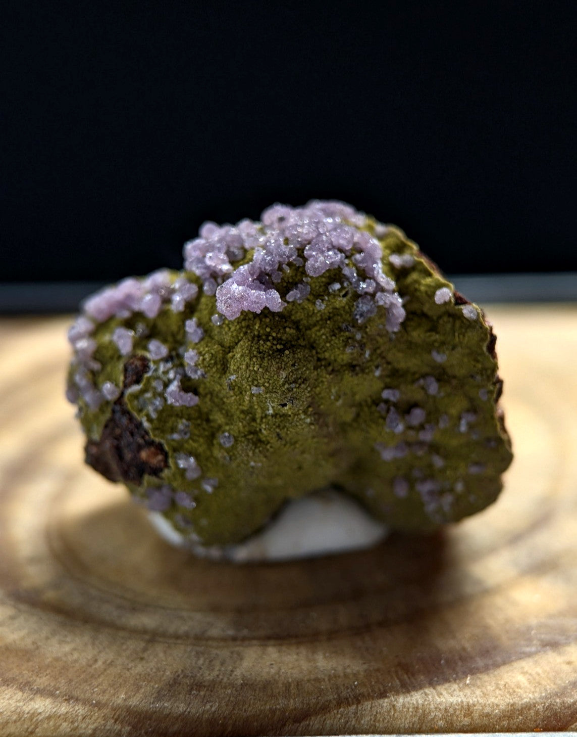 A striking green mineral specimen adorned with delicate, crystalline purple formations.