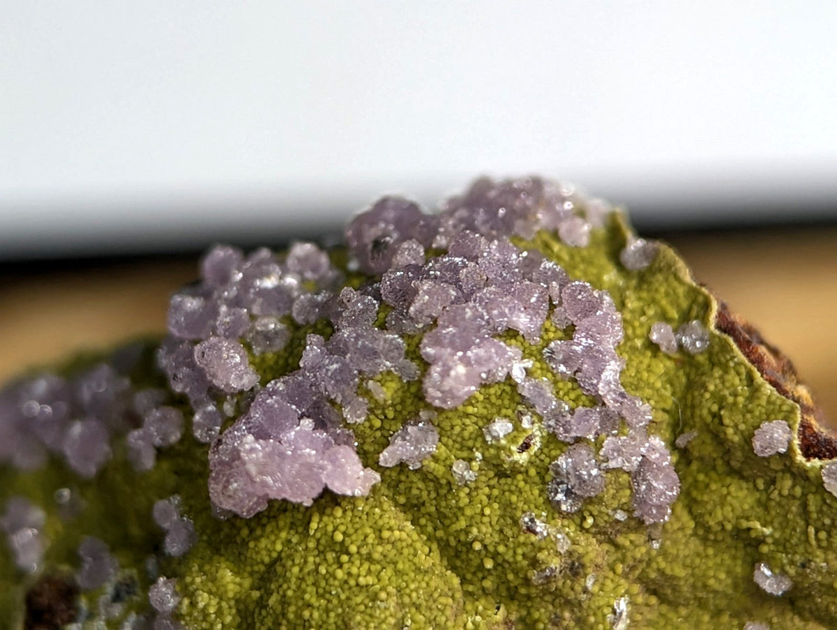 A cluster of translucent, lavender-hued crystals grows densely across a textured green surface.
