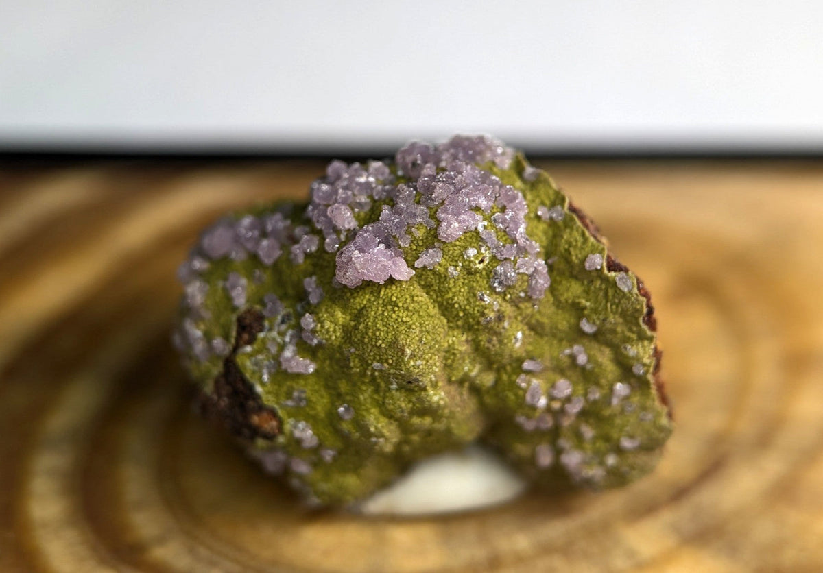 A vibrant green mineral specimen adorned with delicate, crystalline purple formations.