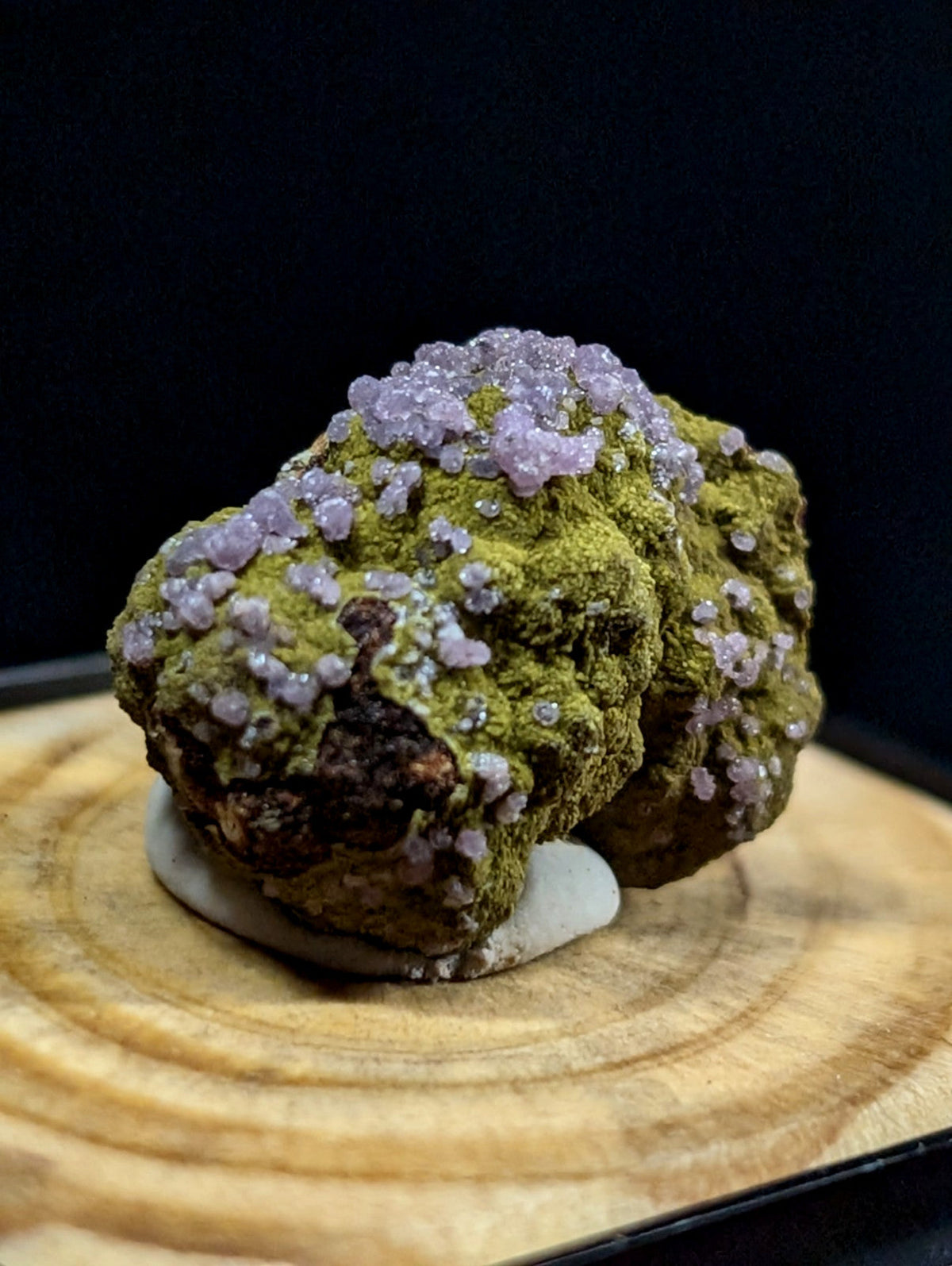 A mossy green mineral specimen adorned with clusters of delicate lavender crystals.