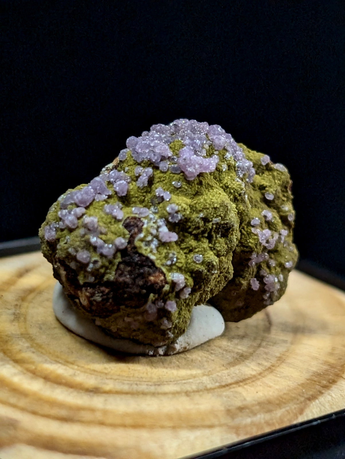 A mossy green mineral specimen adorned with clusters of delicate lavender crystals.