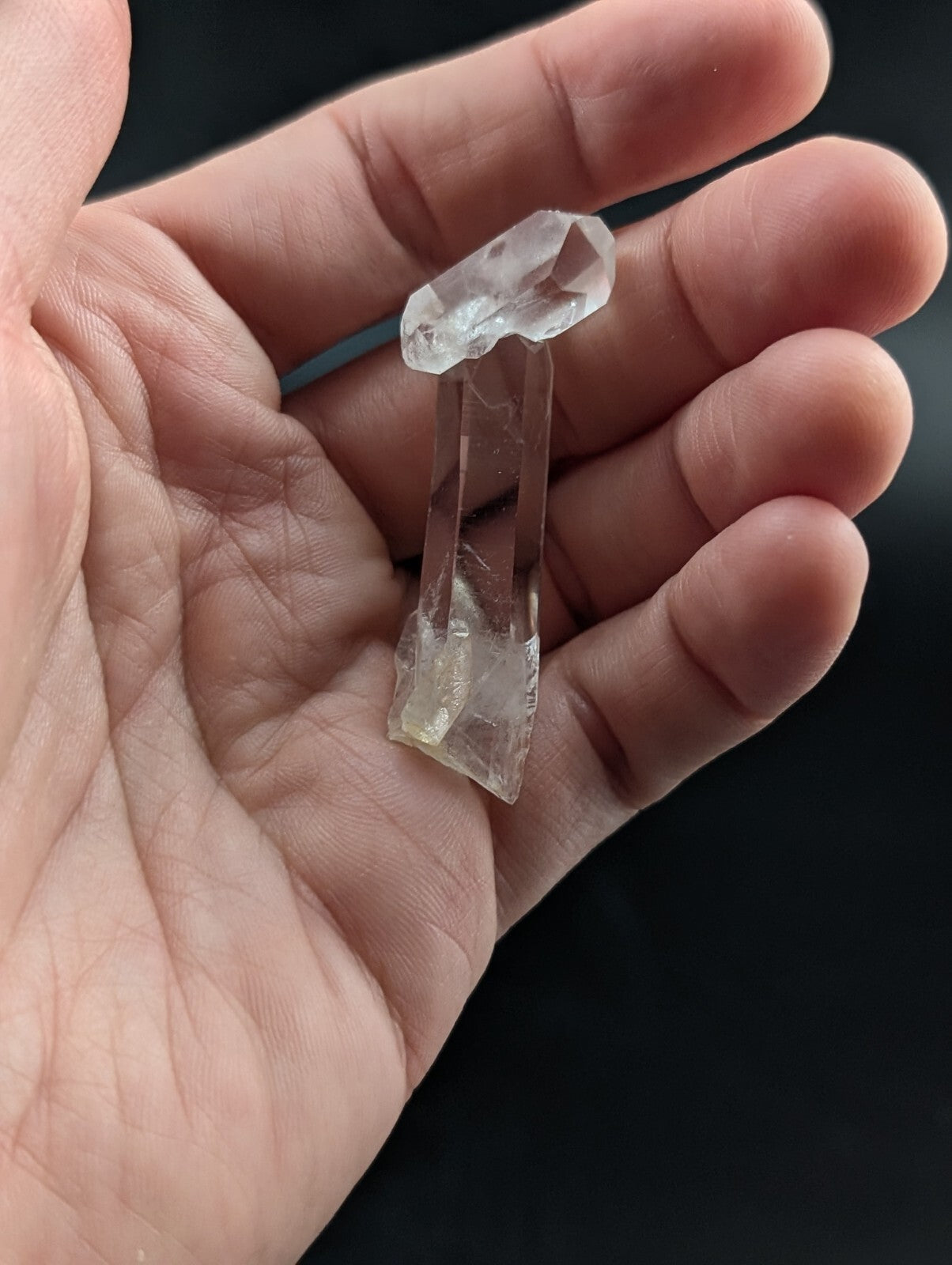 A clear, translucent quartz crystal formation with a pointed top and elongated base.