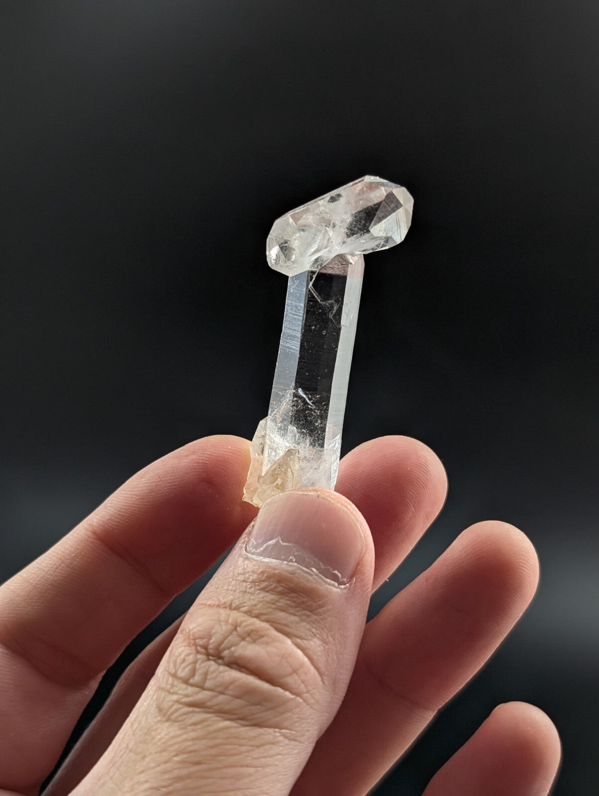 A clear, faceted quartz crystal with a pointed top and translucent body held gently in someone’s hand.