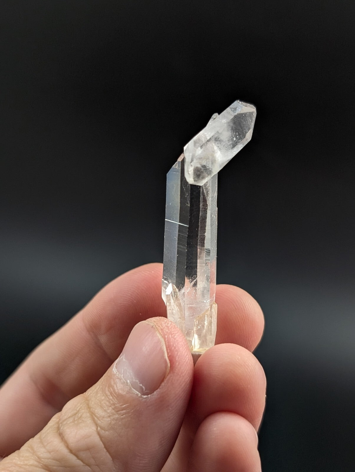 A clear quartz crystal with a tall, faceted column and a smaller, pointed crystal growing from its top.