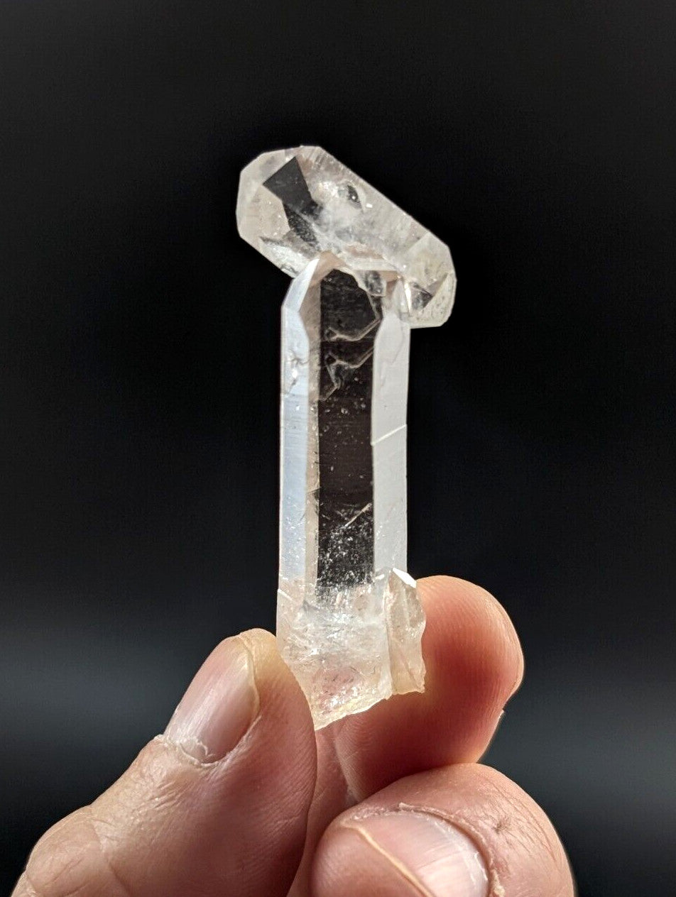 A clear, translucent quartz crystal with a distinct vertical column and a faceted top.