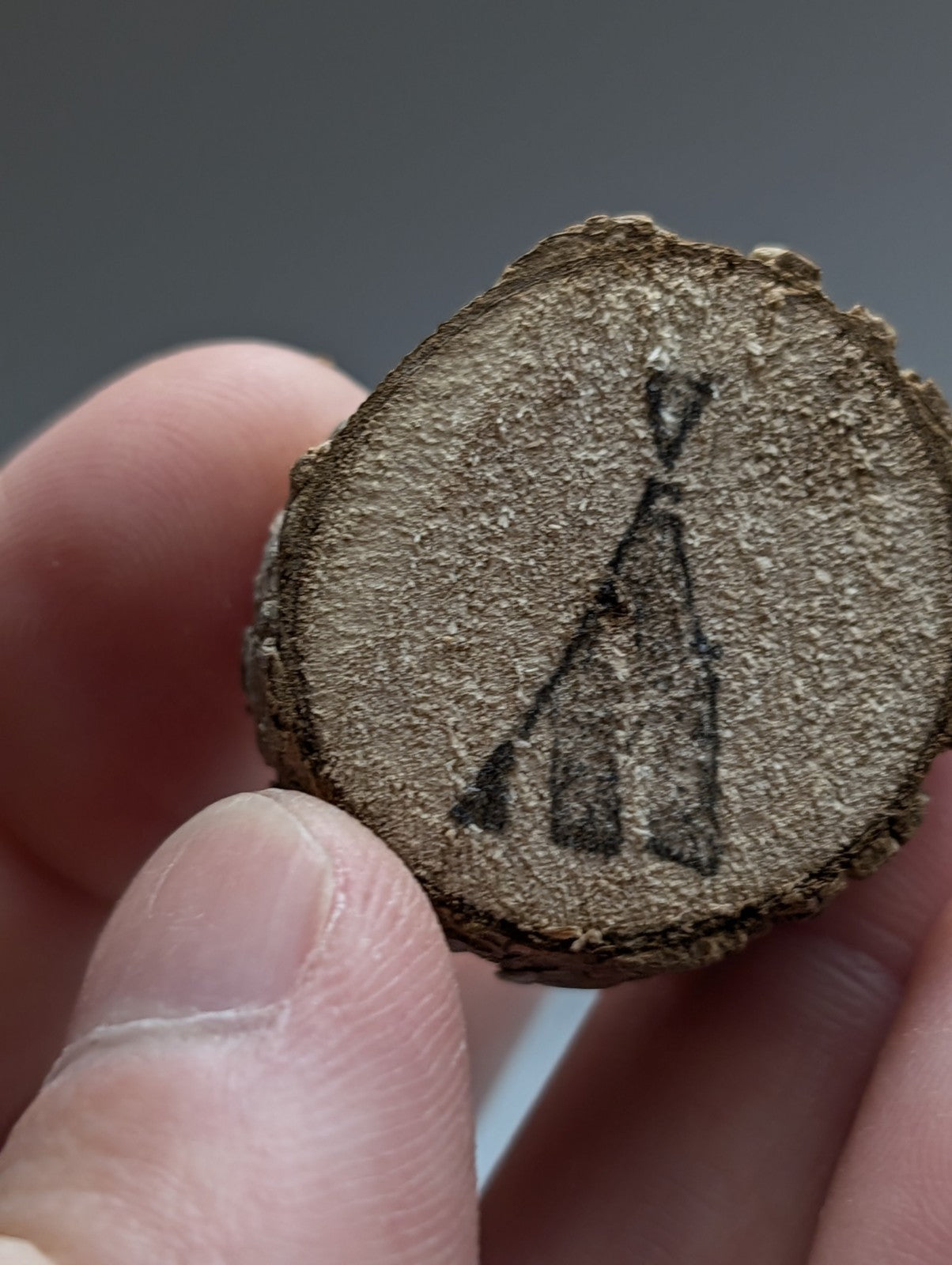 A rustic circular wooden slice with natural brown bark and dark charcoal teepee engraving on a natural wood base