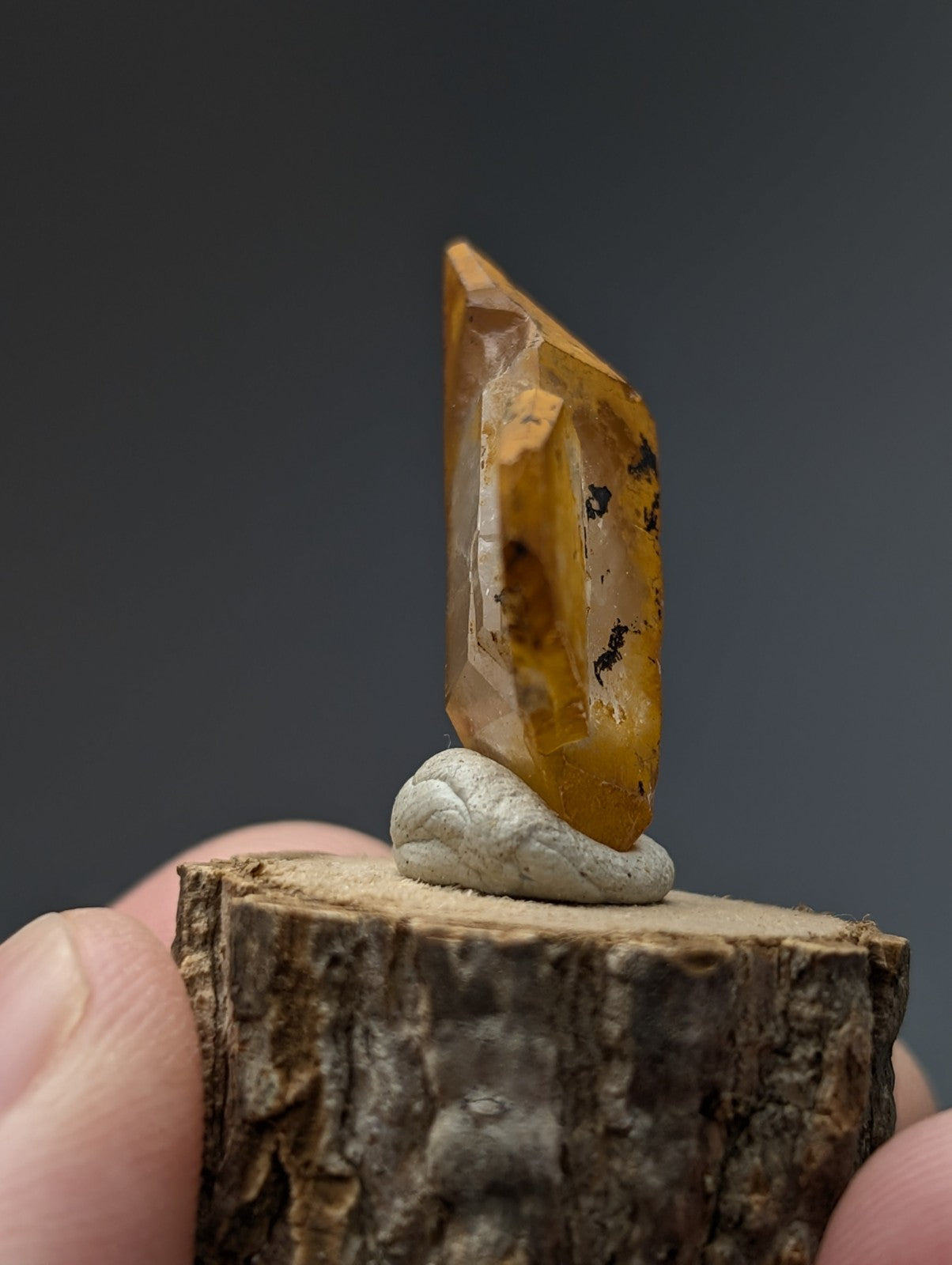 A translucent amber-colored quartz crystal with natural inclusions displayed upright on a white stone base