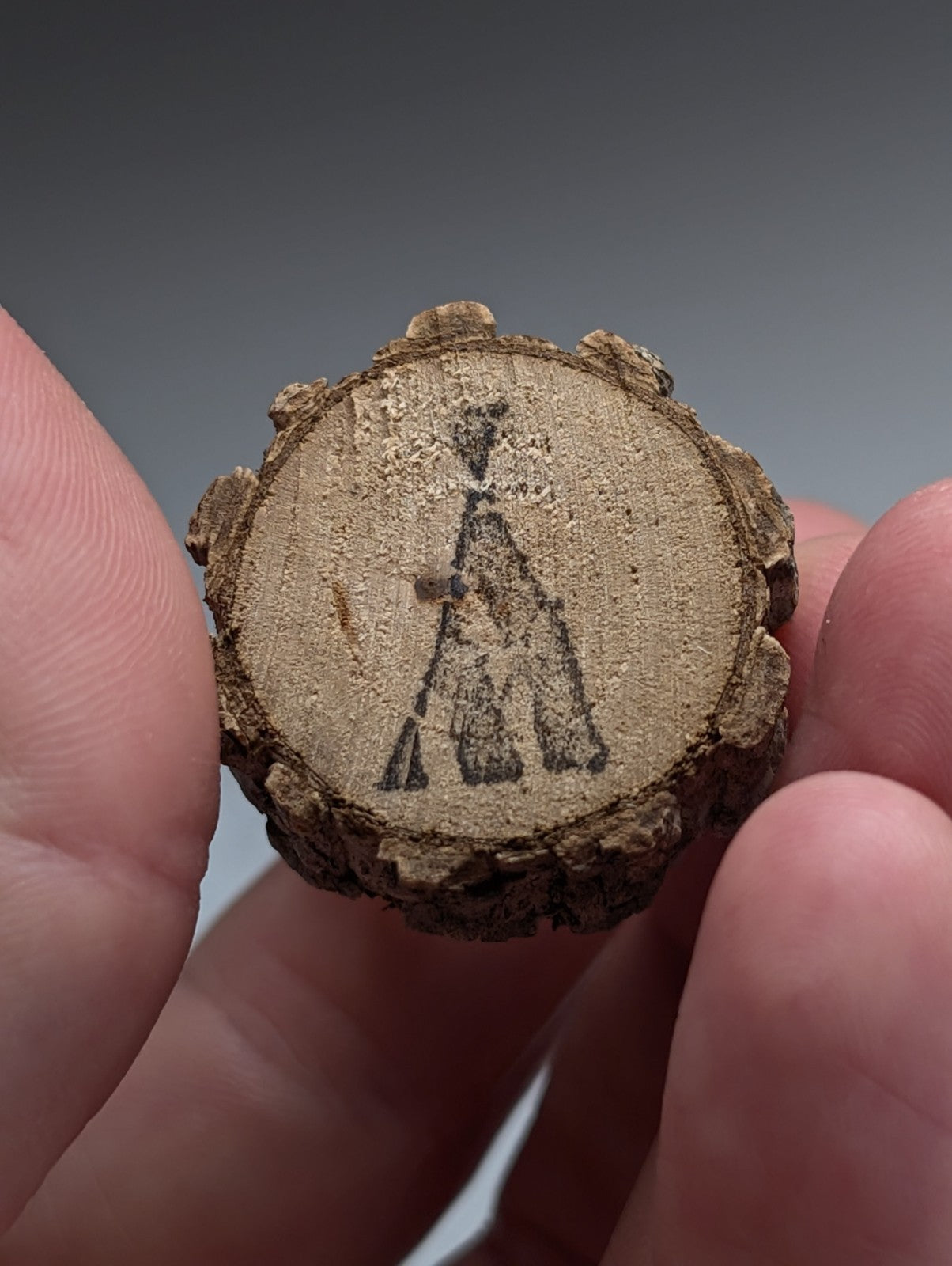 A rustic circular wooden slice with bark edge and carved teepee design on natural wood base from garland county quartz