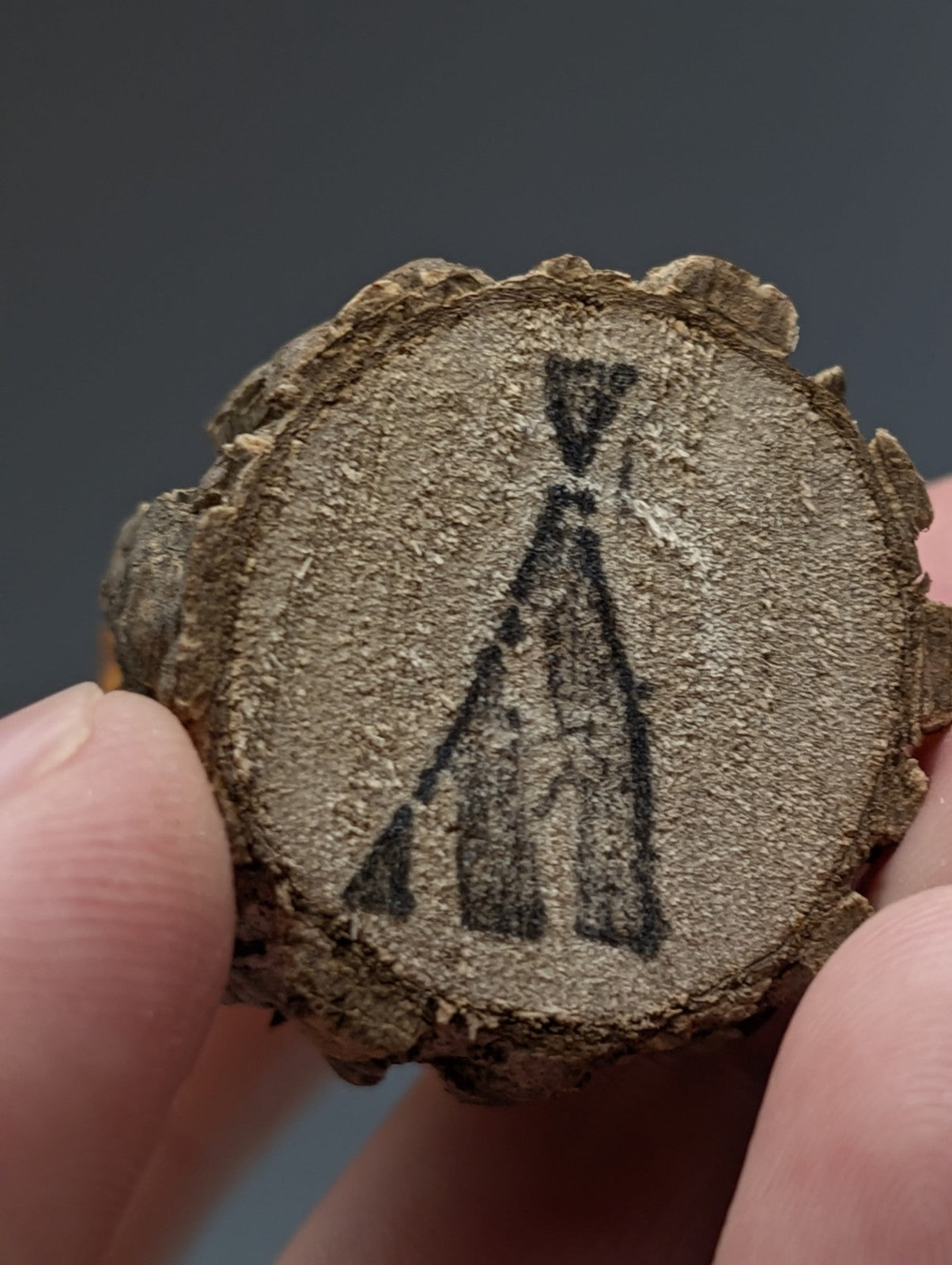 A rustic circular wooden slice with natural bark and hand-drawn black teepee on a wood base for a unique quartz display