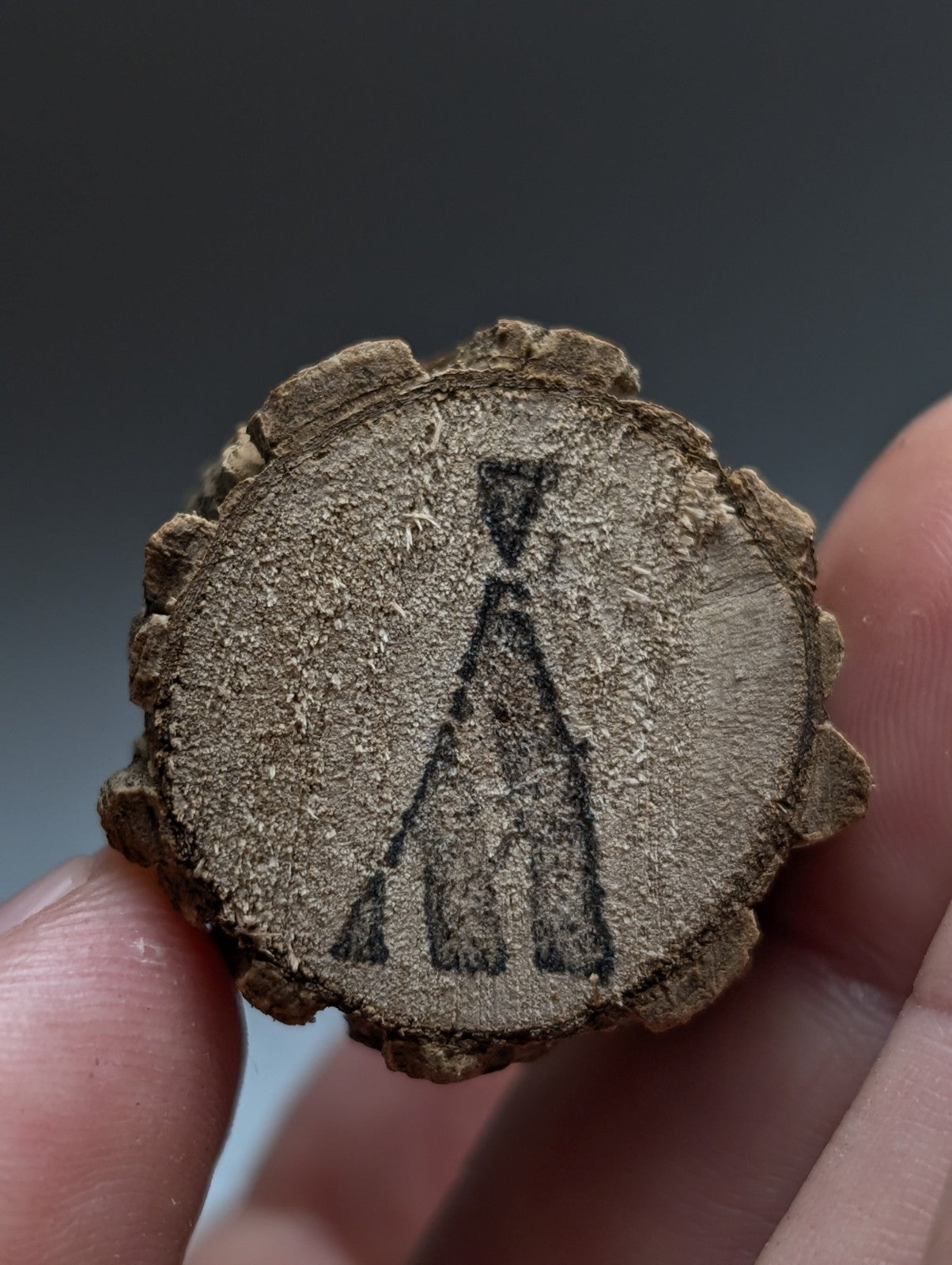 A rustic circular wooden slice with bark edge and black hand-drawn teepee design on natural wood base from garland county arkansas quartz