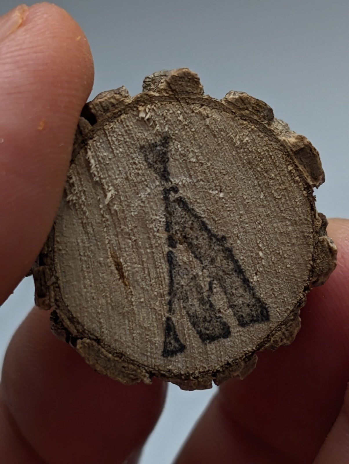 A rustic circular wooden slice with natural bark edge and black tribal engravings on a natural wood base