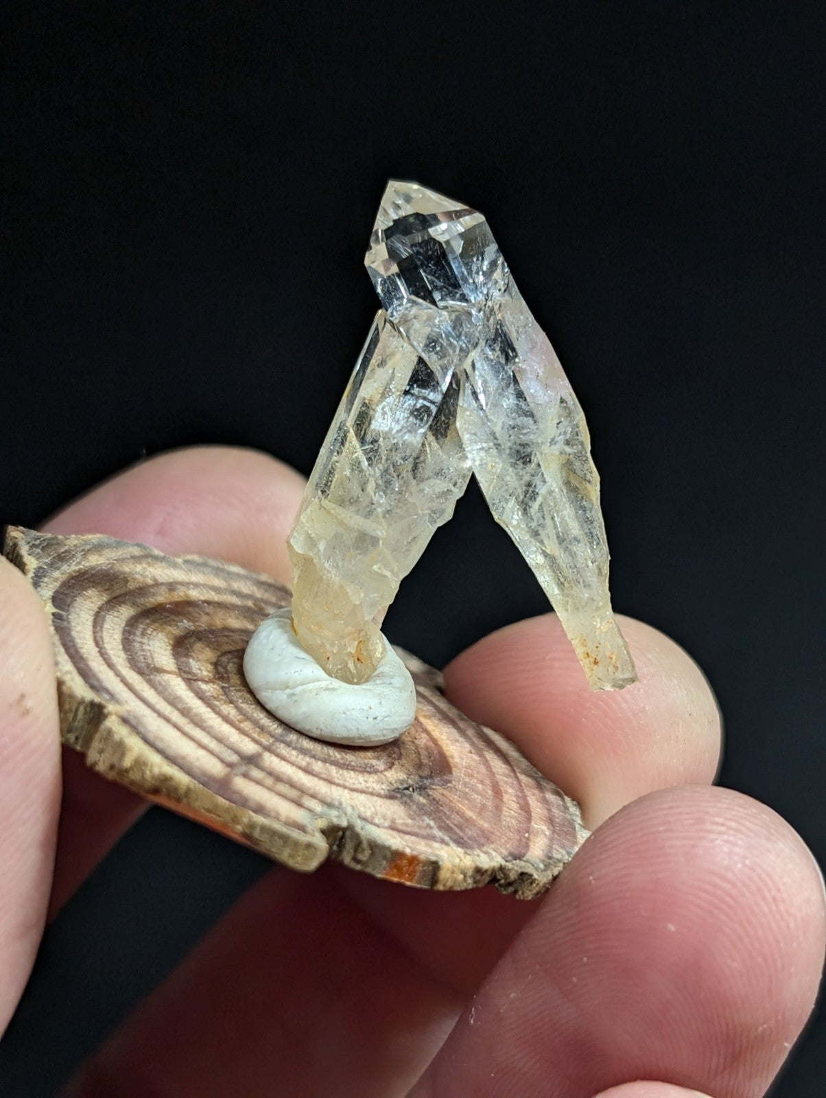 A translucent, faceted quartz crystal formation with a pale yellowish tint stands upright on a circular wooden slice base.