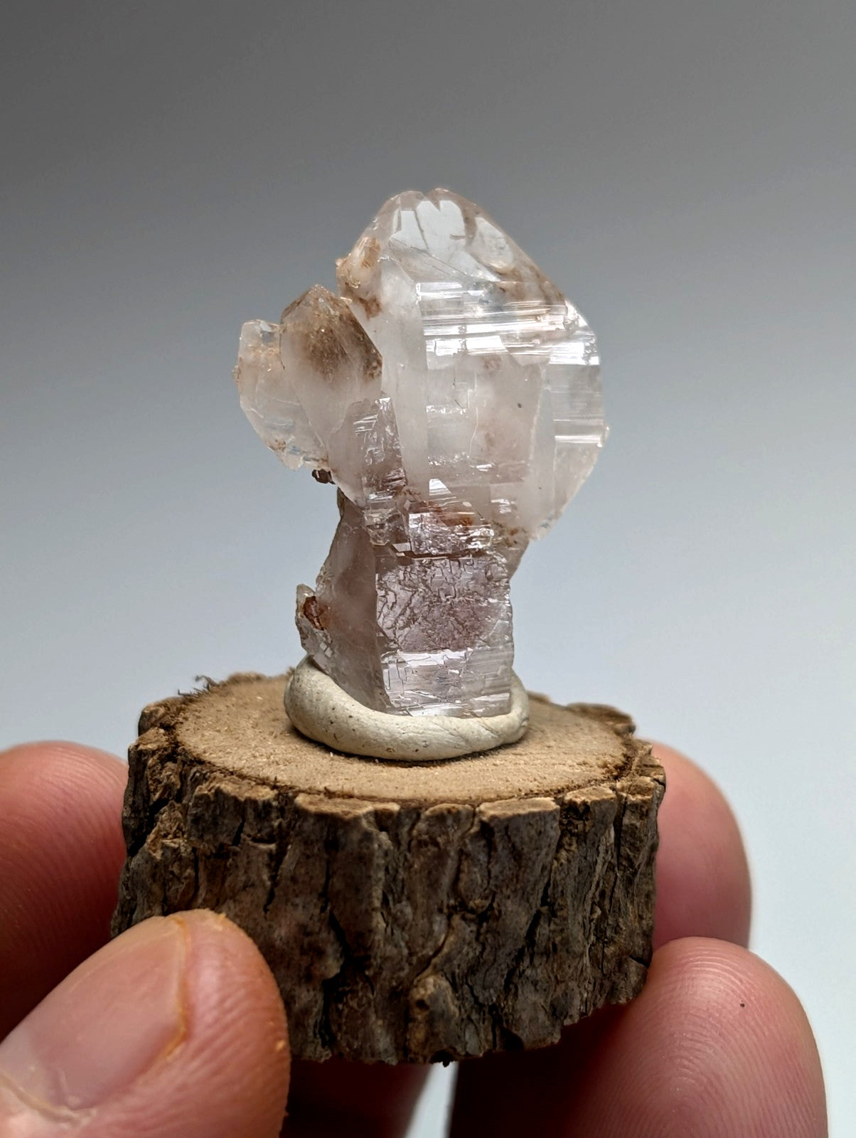A unique translucent quartz specimen with pink hues and faceted structure on a natural wood base from montgomery county arkansas