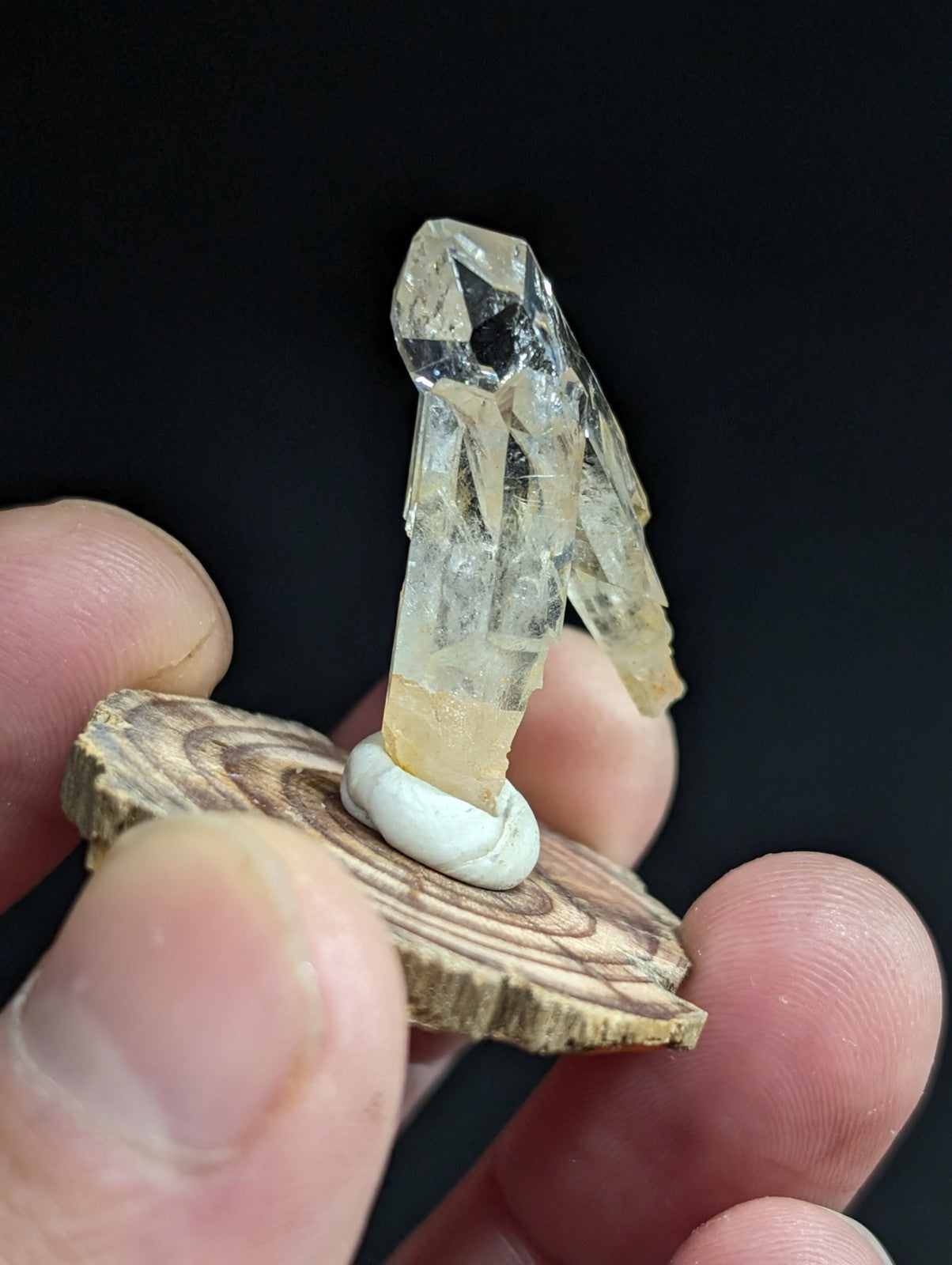A translucent, pale yellow crystal geode with a faceted, angular structure mounted on a circular wooden base.
