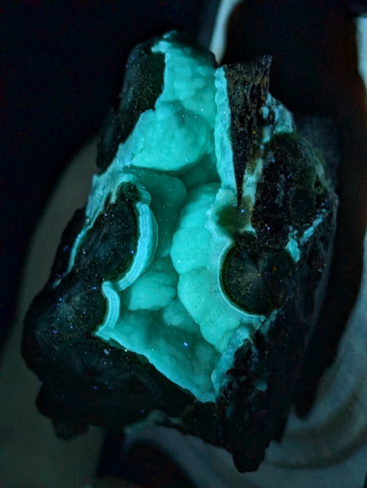 A glowing turquoise geode with a dark, rugged exterior and crystalline interior.