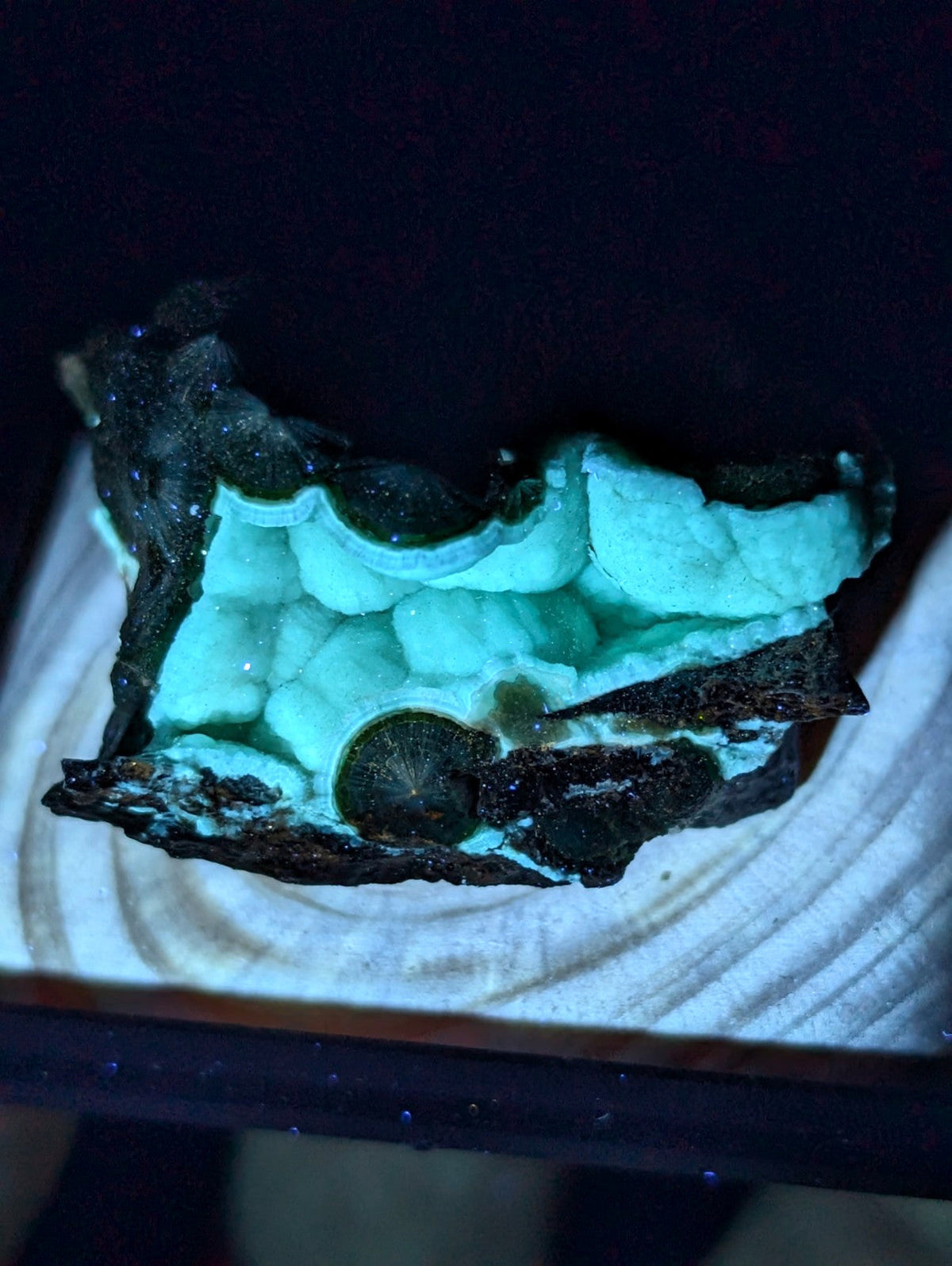A glowing turquoise mineral specimen with a dark, textured outer shell and an inner crystalline structure.
