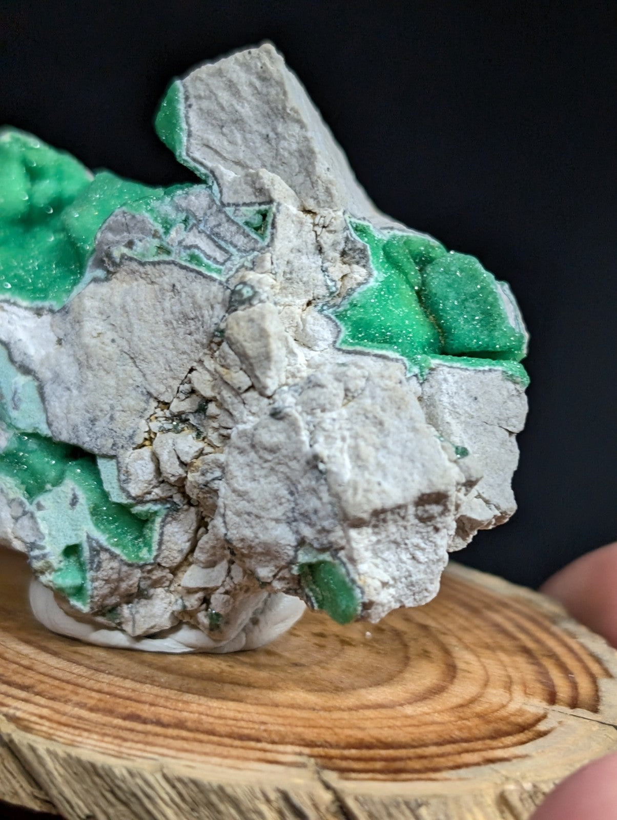 A striking green malachite mineral specimen with a crystalline, glittering surface set against a contrasting gray rock matrix.