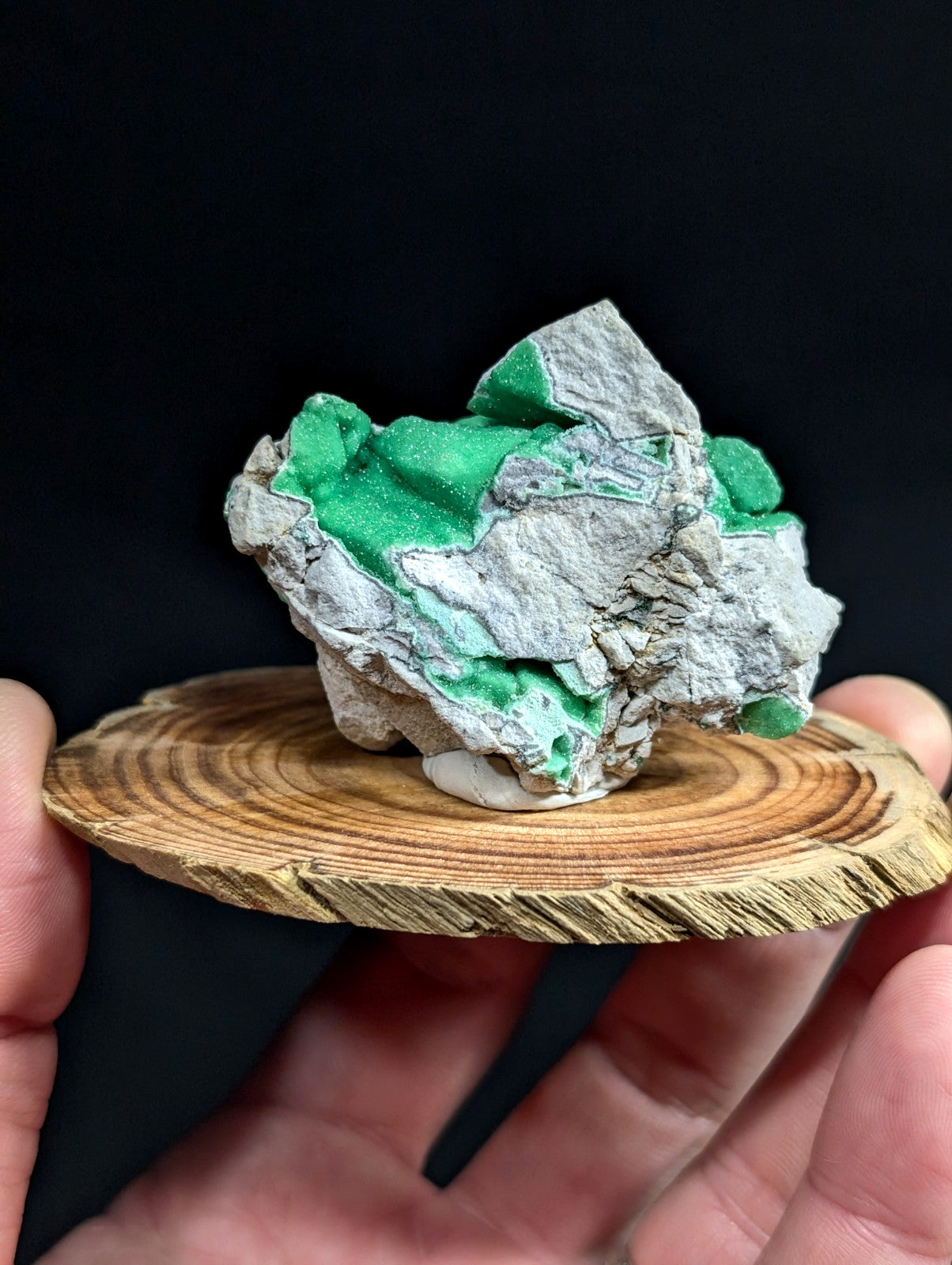 A vibrant green mineral specimen with a rough, textured surface set against a grayish rock matrix.