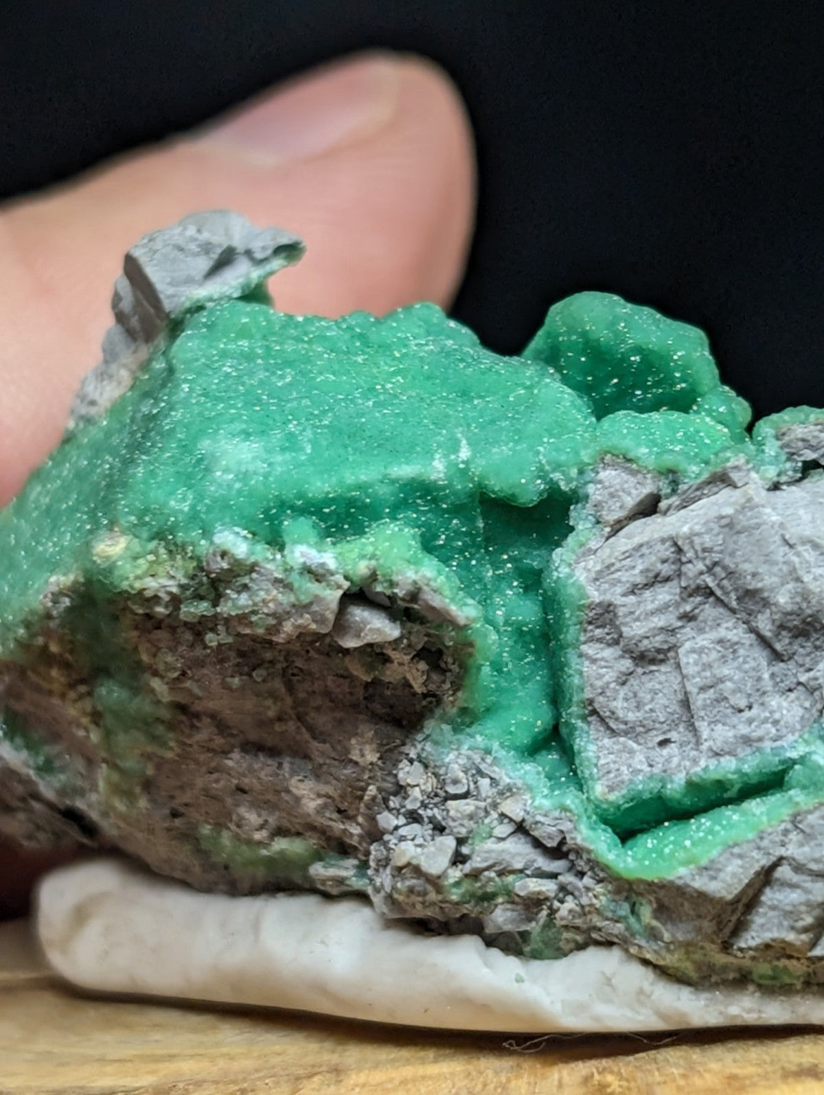 A vibrant green, crystalline mineral specimen with a rough, textured surface and gray rock matrix.
