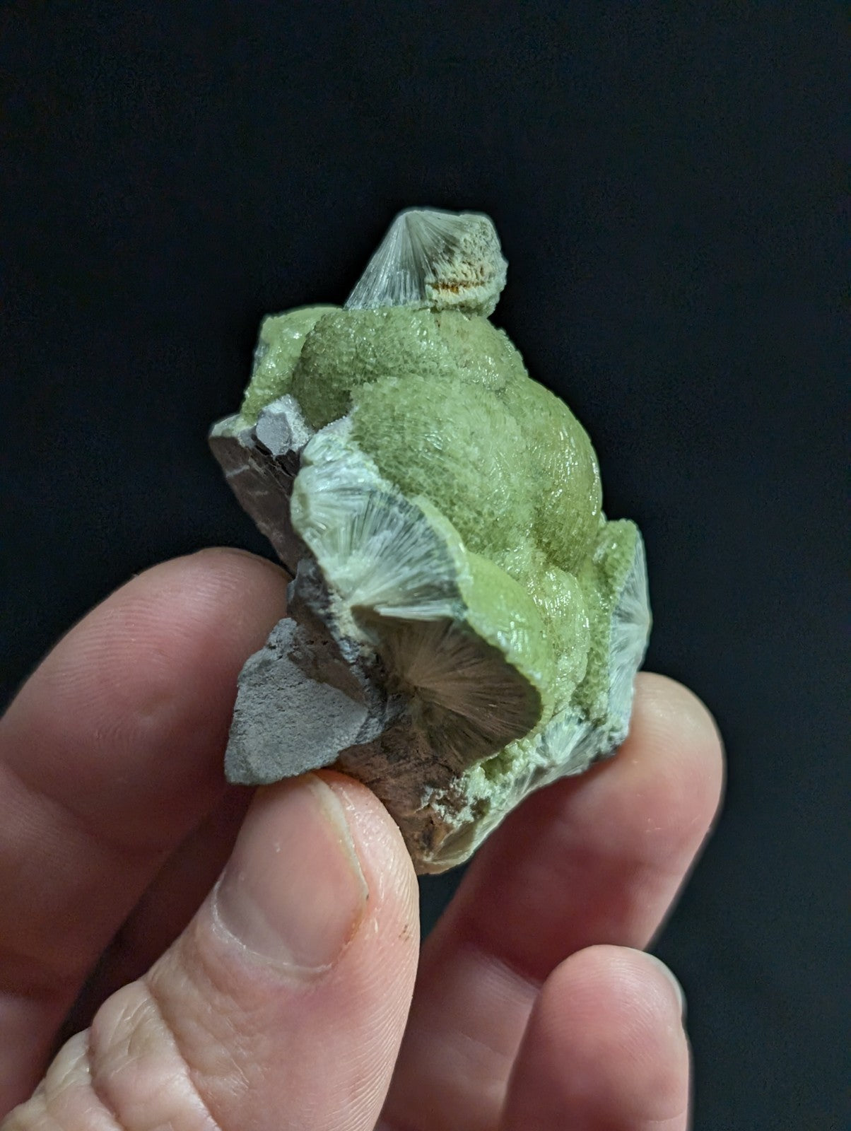 A green, textured mineral specimen with a rough, irregular surface and some translucent white crystalline formations.