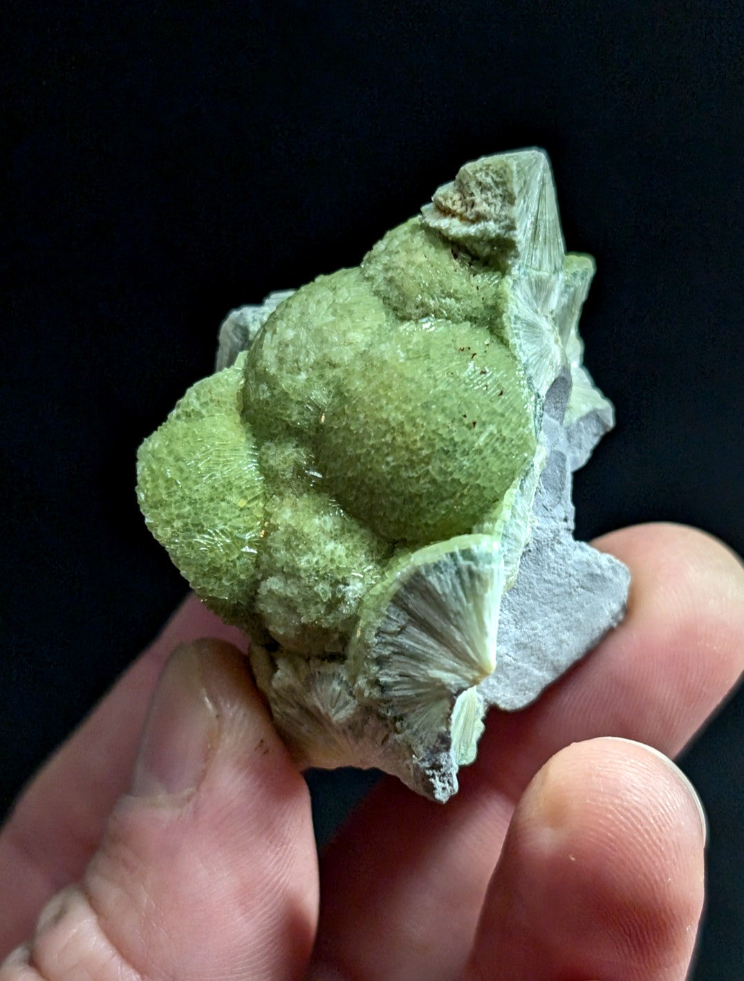 A hand holds a green, textured mineral specimen with crystalline formations and layered surfaces.