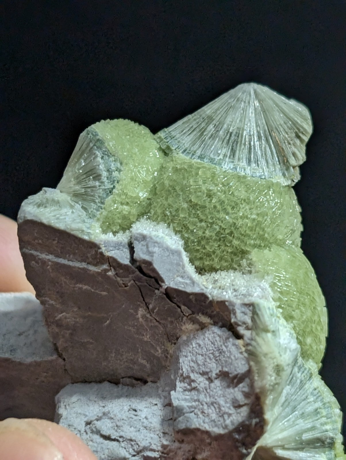 A striking green and translucent mineral specimen featuring a conical, fan-like crystal formation atop a textured matrix of earthy brown and gray rock.