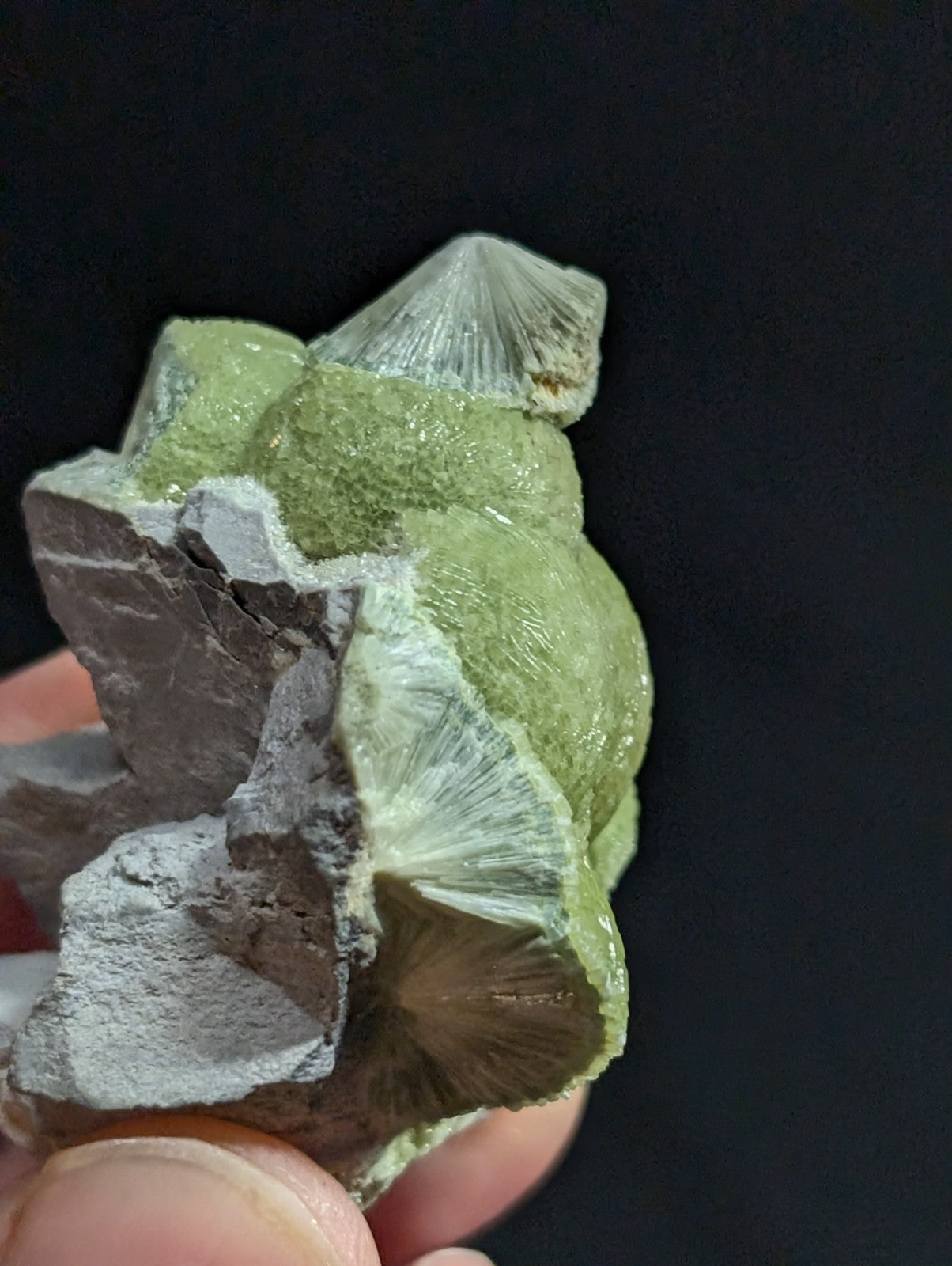 A green, crystalline mineral specimen with a rough, textured surface and translucent, fan-like crystal formations.
