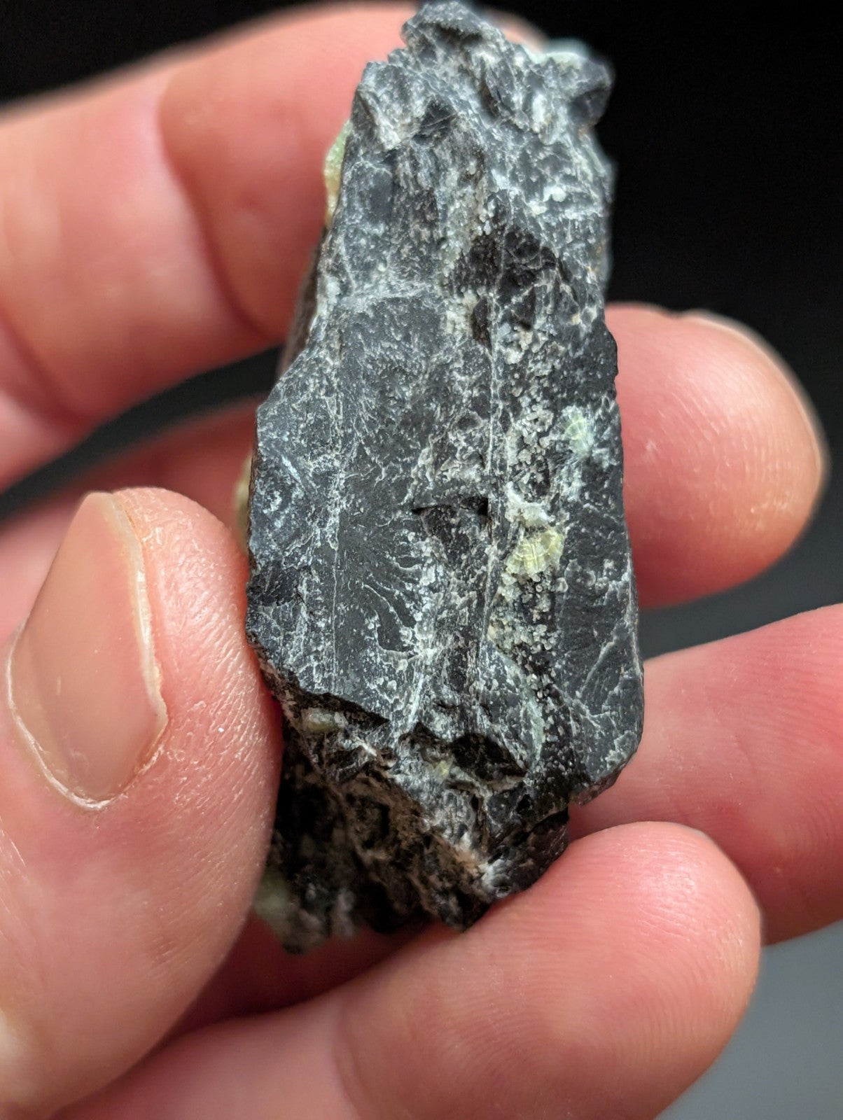 A rugged, dark gray rock with a rough texture and subtle greenish veining.