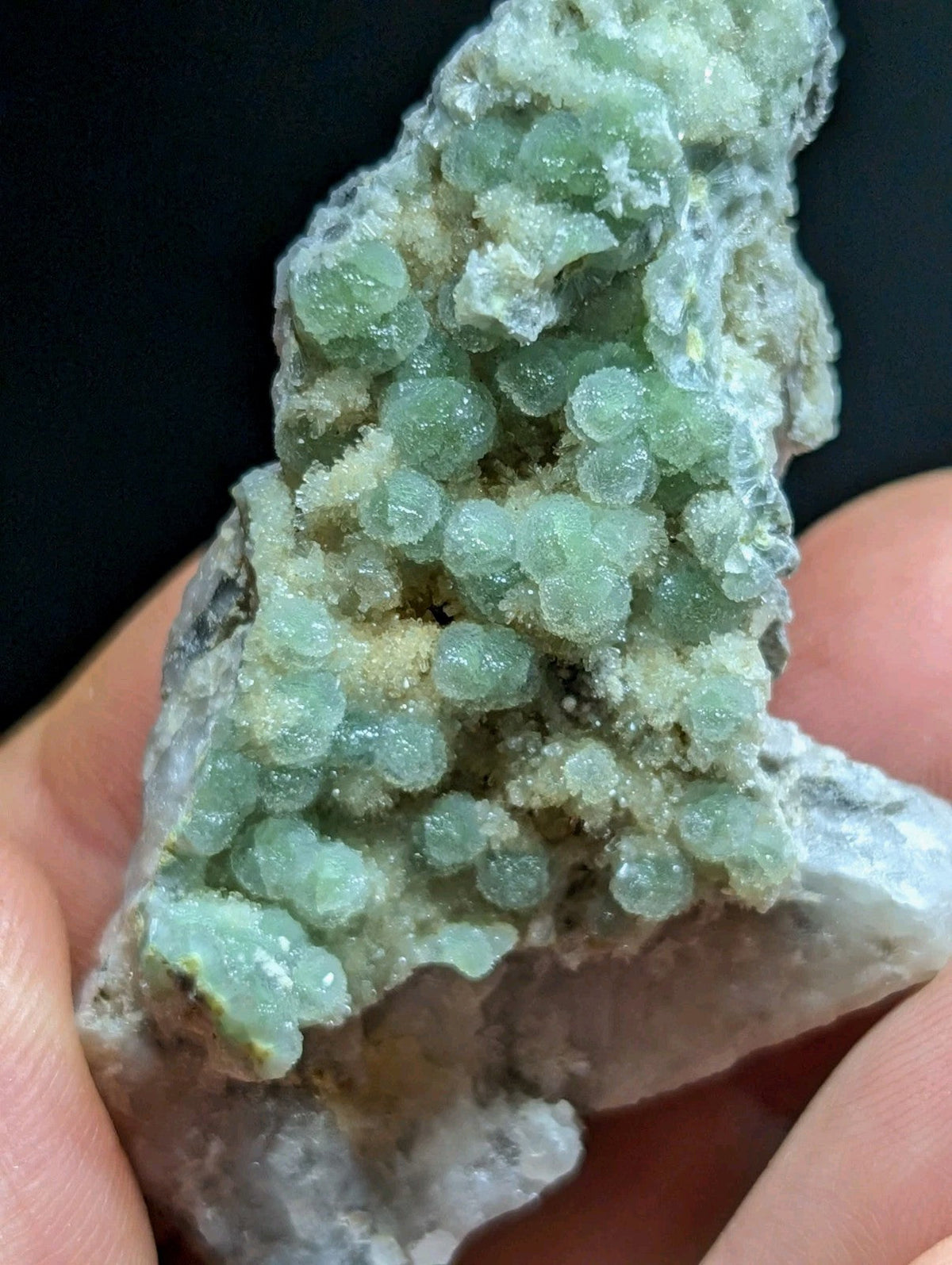 A cluster of translucent green, bead-like crystals growing from a rough gray rock matrix.