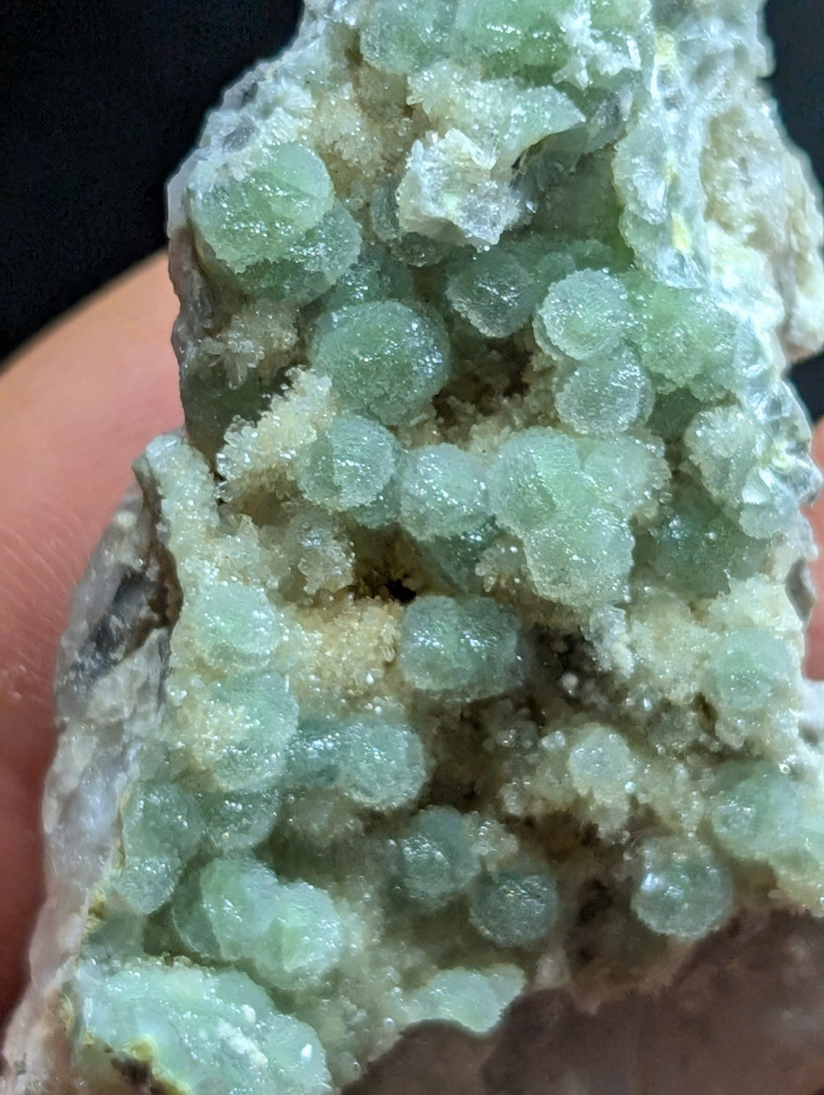 A cluster of translucent, light green spherical crystals growing from a rough, earthy matrix.