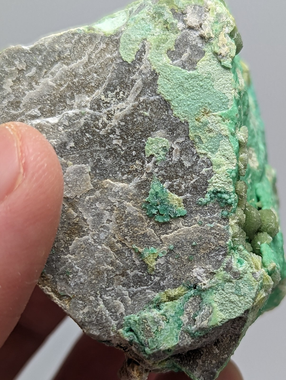 A rough, irregularly shaped mineral specimen with a mottled surface of gray rock and vibrant green patina.
