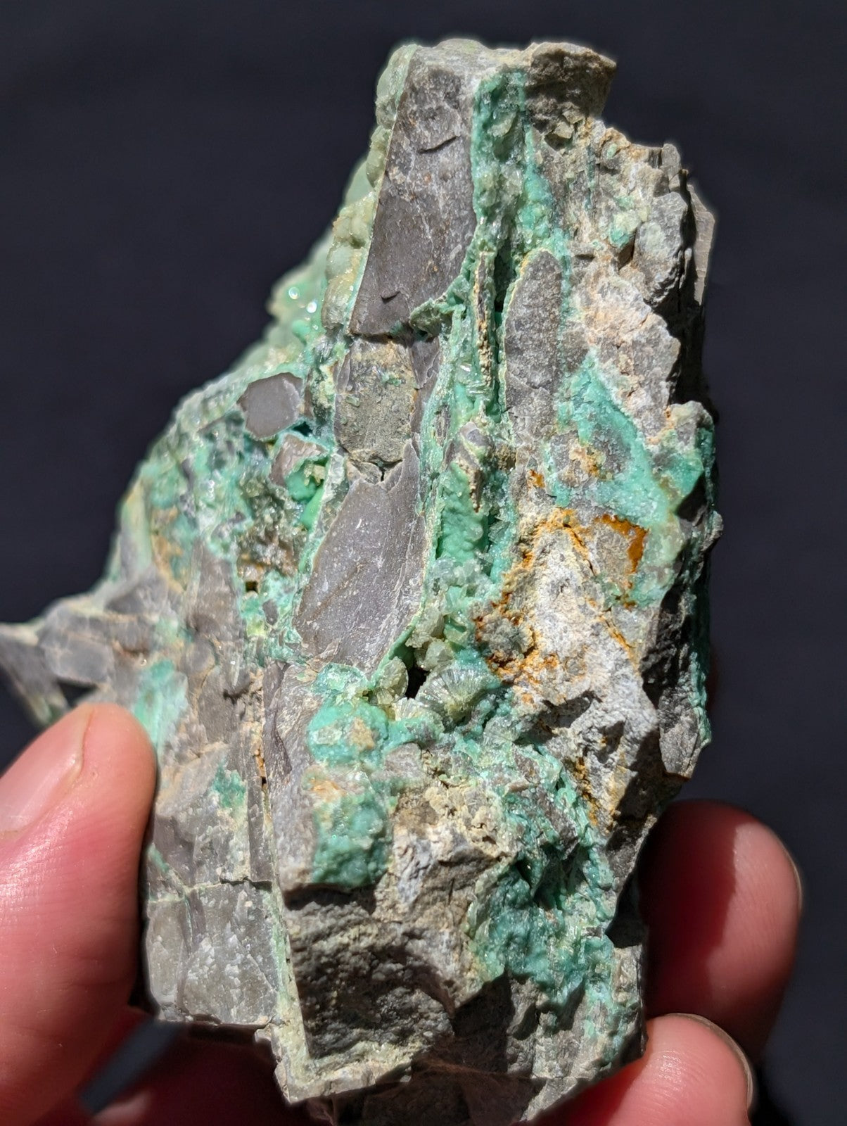 A rough, irregularly shaped mineral specimen with vibrant green patches and grayish rock matrix.
