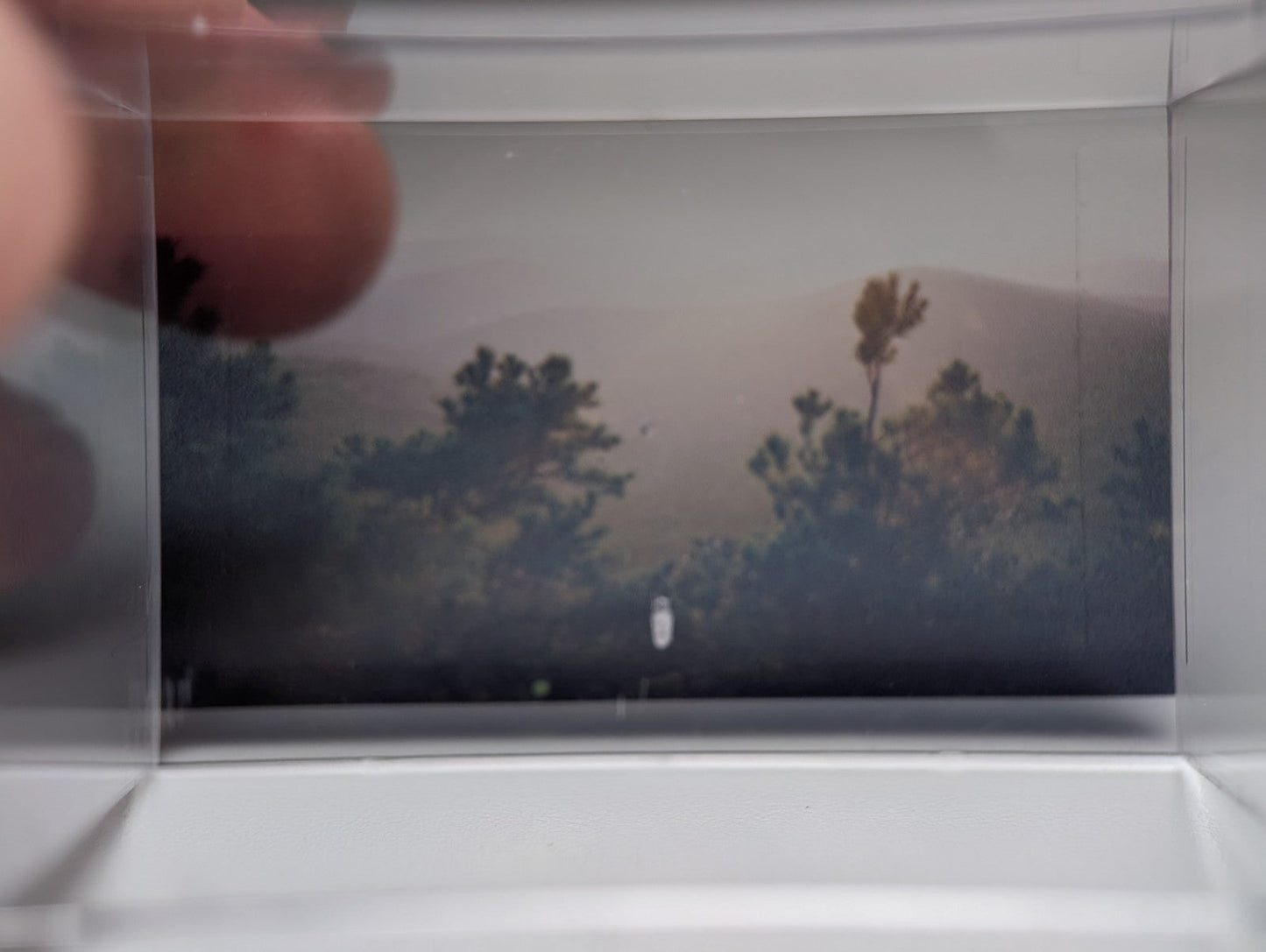 A clear plastic photo frame holding a muted landscape image with silhouetted trees in a rare a plus wavellite on variscite case