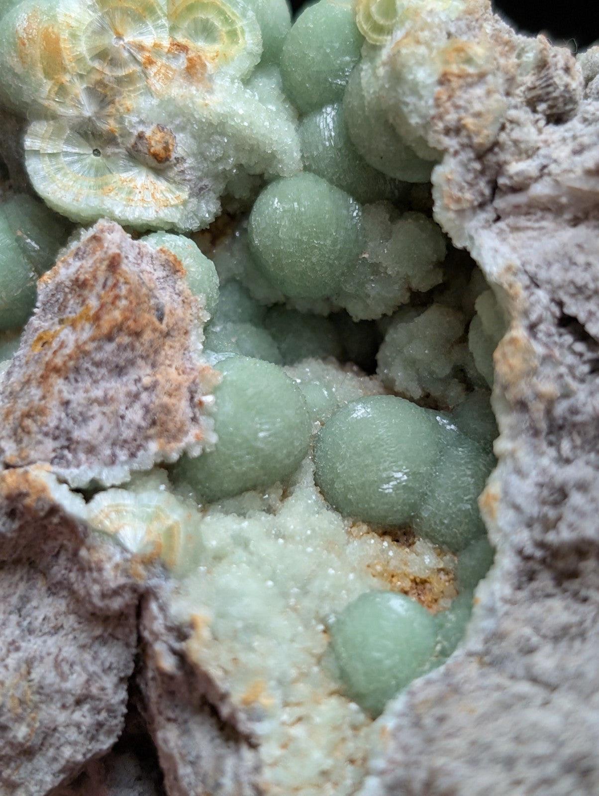 A cluster of translucent, pale green spherical crystals nestled within a rough, earthy matrix.