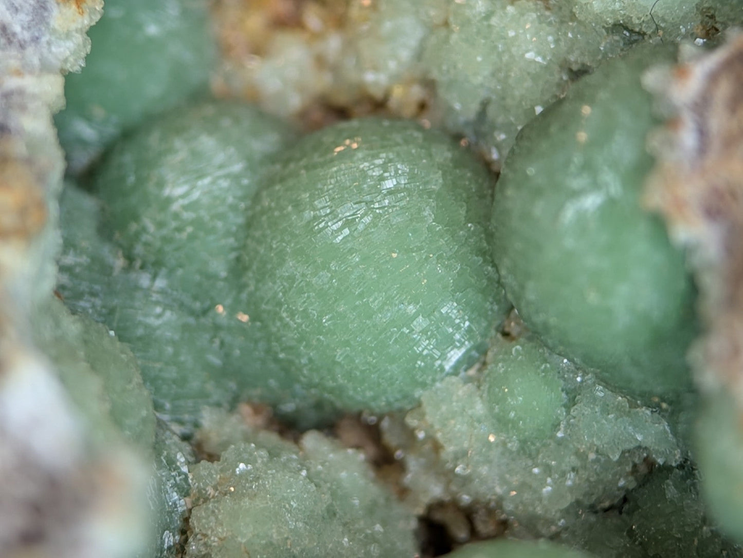 Spherical, translucent green mineral crystals nestled within a rougher matrix of crystalline rock.