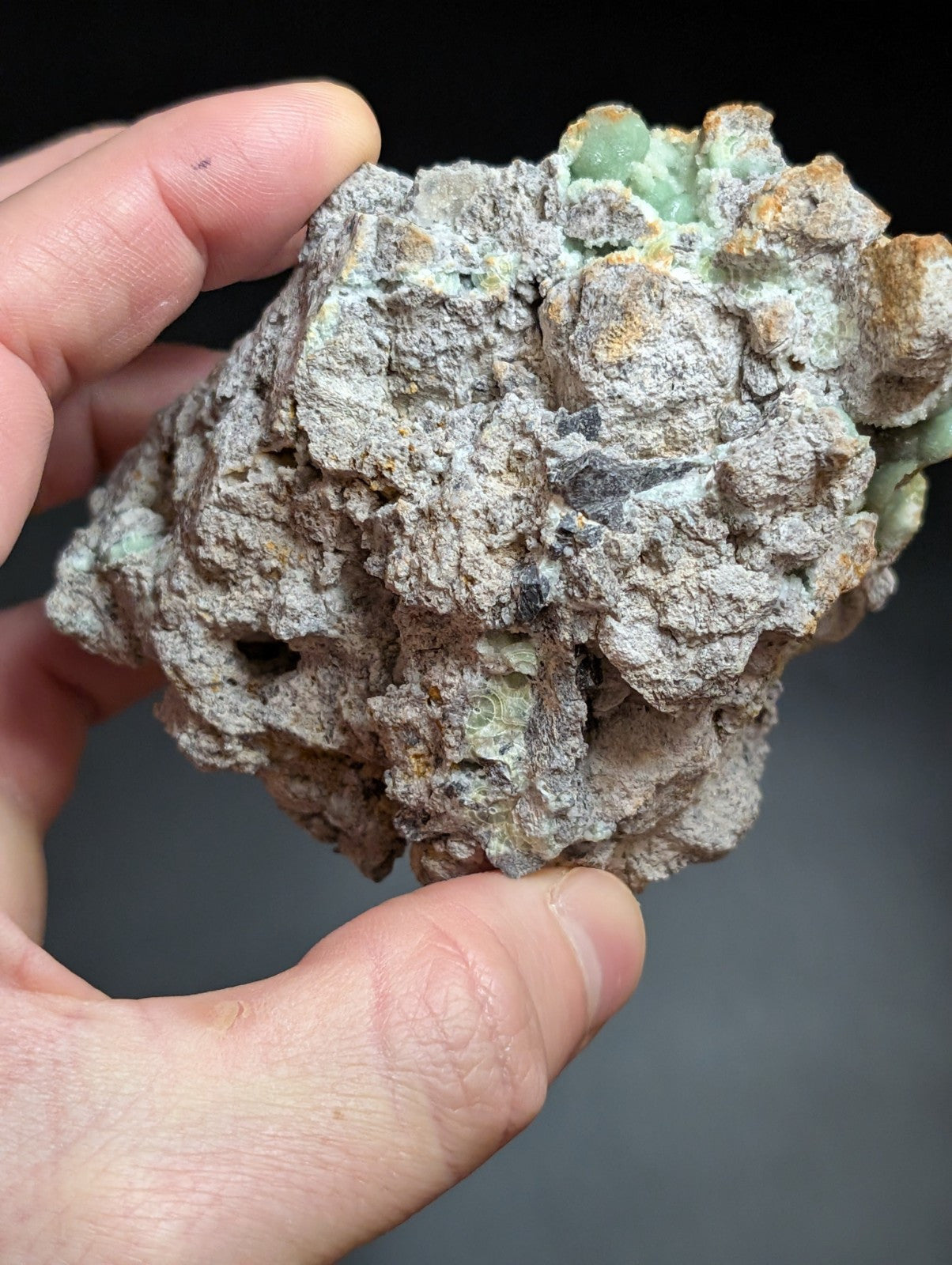A rough, irregularly shaped mineral specimen with a textured surface displaying patches of pale green and earthy brown tones.