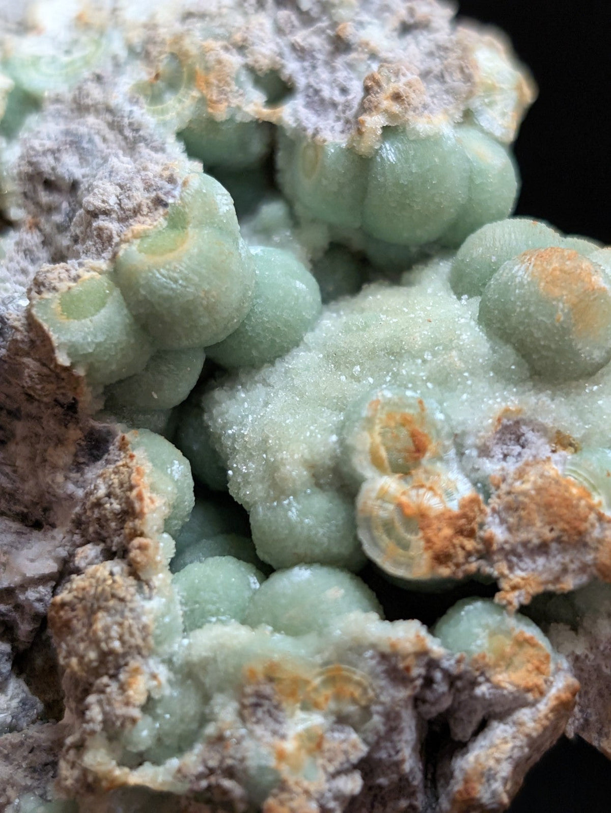 A cluster of translucent green, spherical mineral formations with a crystalline texture and patches of orange-brown oxidation.