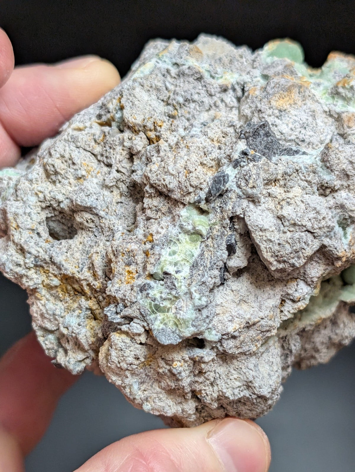 A rough, irregularly shaped mineral specimen with a grayish base color and patches of pale green crystalline formations.