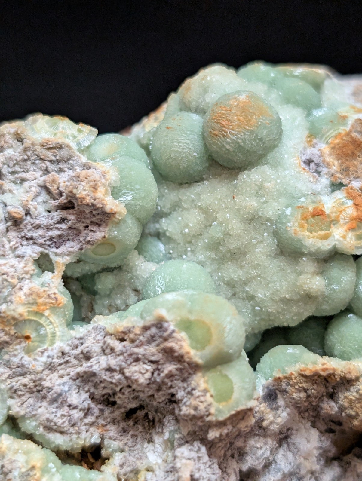 A cluster of pale green, spherical mineral formations with a crystalline texture and subtle orange-brown patches.