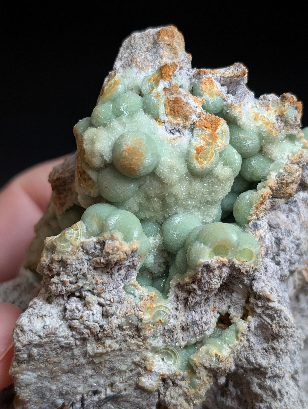 A cluster of translucent, pale green spherical crystals growing from a rough gray rock matrix.