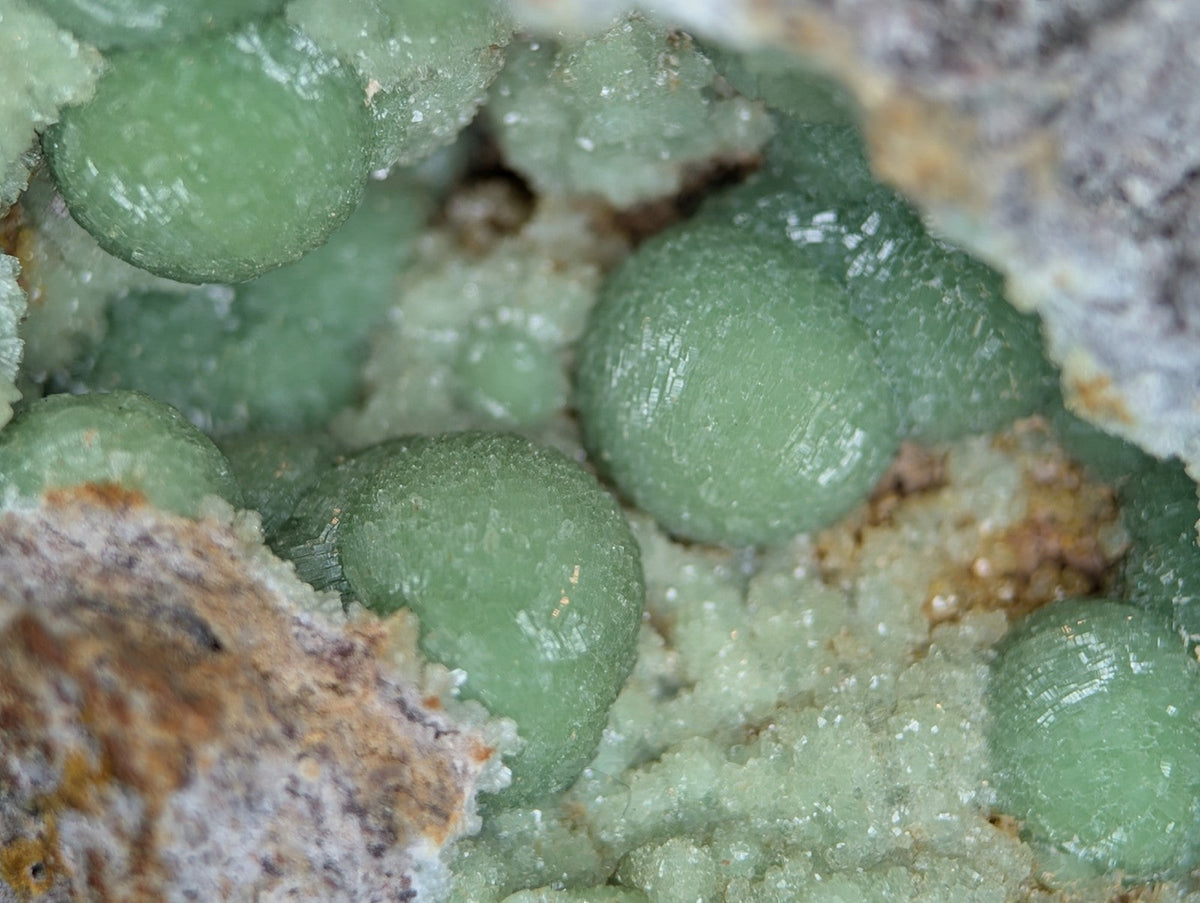Spherical, translucent green mineral formations nestled within a rougher matrix of earthy tones.
