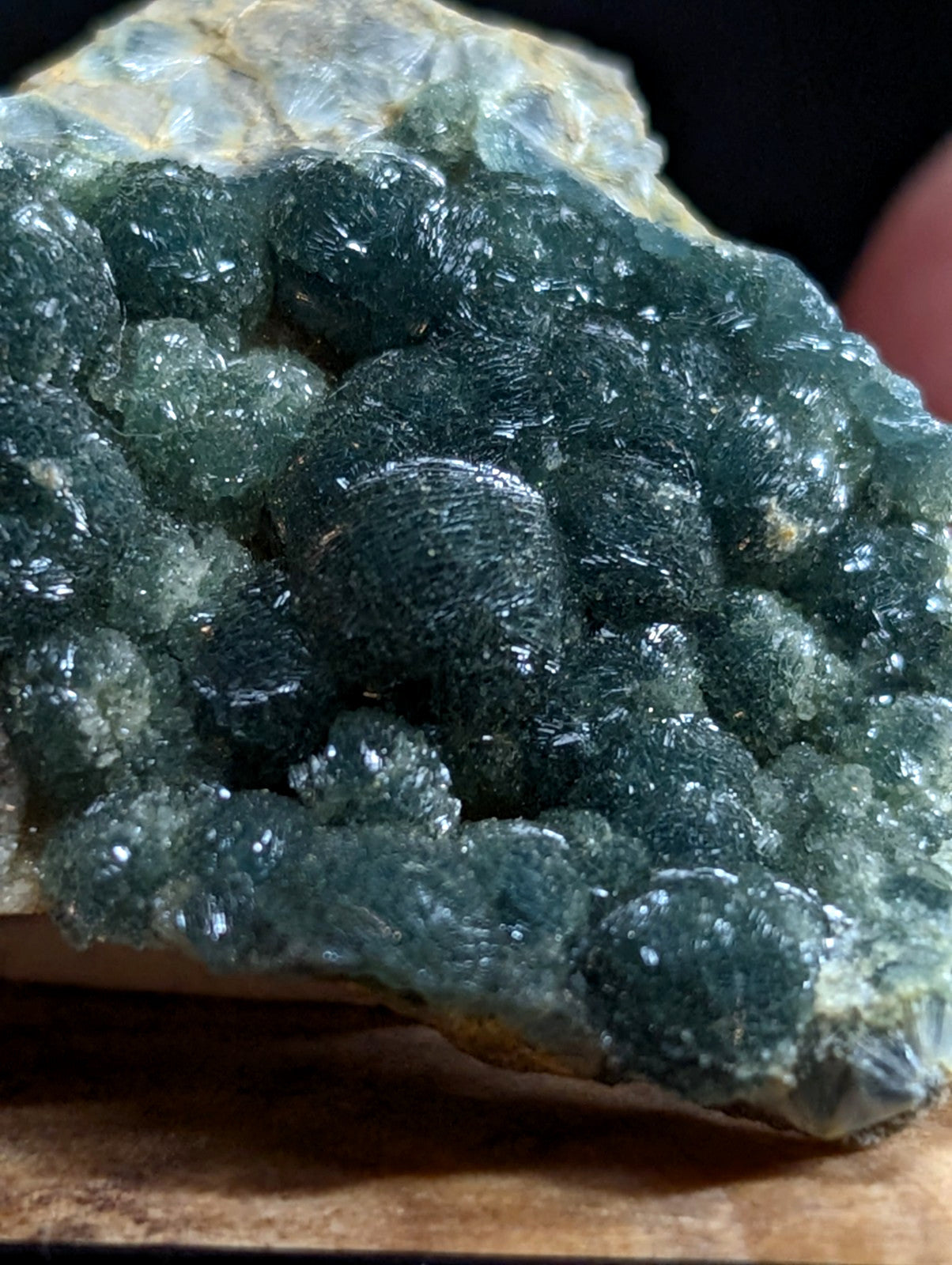 A cluster of deep teal, translucent crystals with a bumpy, rounded surface forms part of an earthy mineral specimen.