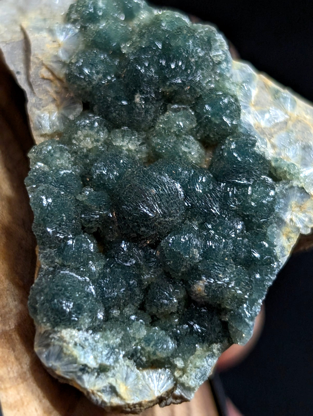 A cluster of deep green, translucent crystals with a rough, bumpy texture grows from a lighter-colored rock base.